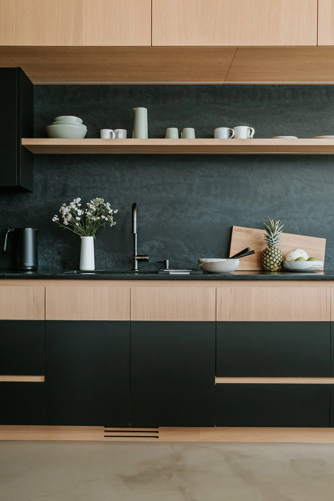 Sunstone Straight-on kitchen view: dark stone backsplash, oak upper cabinets, exposed shelf — new-build interior design in Pemberton, BC by LRD Studio. Photography by Darby Magill.