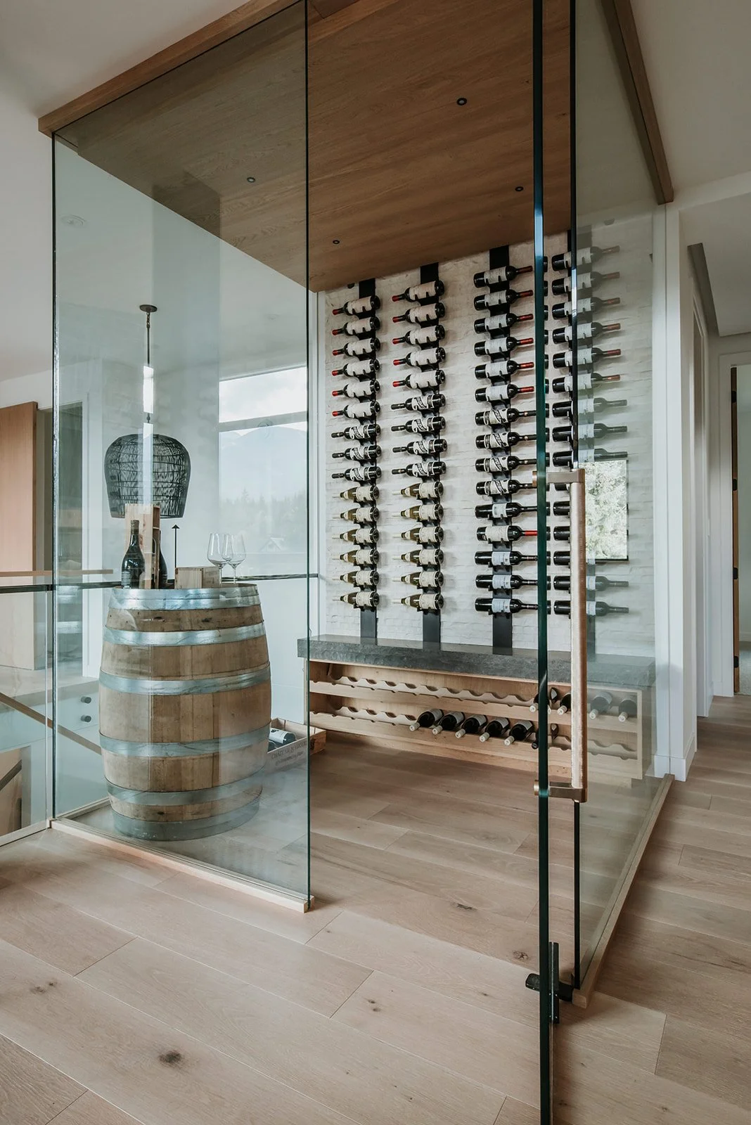 Balsam Glass-enclosed wine room: bottles on vertical wall-mount racks, wine barrel — new-build interior design in Whistler, BC by LRD Studio. Photography by Darby Magill.