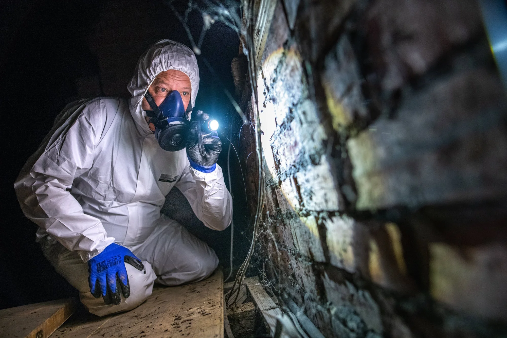 Man in a full protective suit and breathing equipment surveying an attic