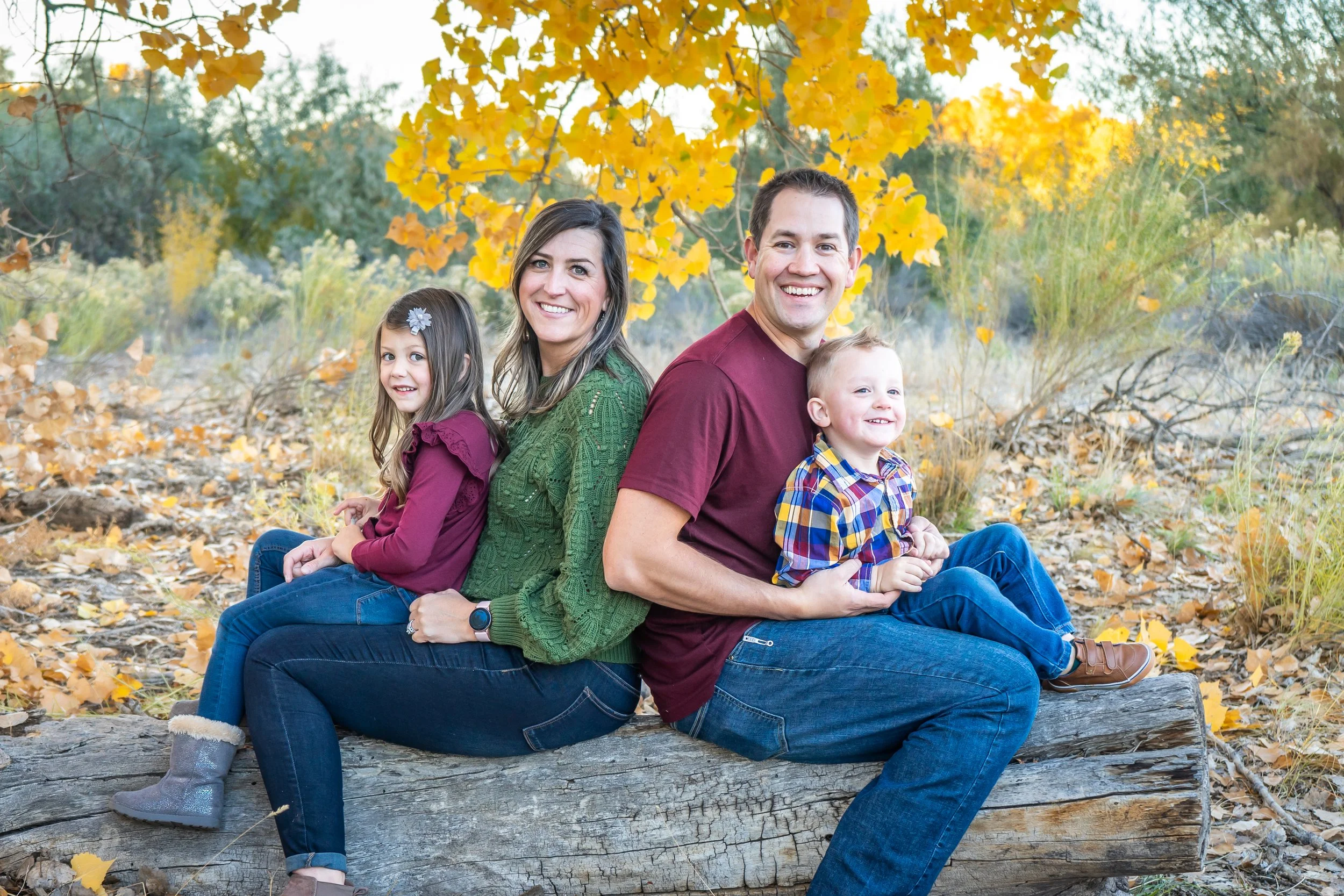 The Powell Family is sitting together on a log with the fall leaves behind them