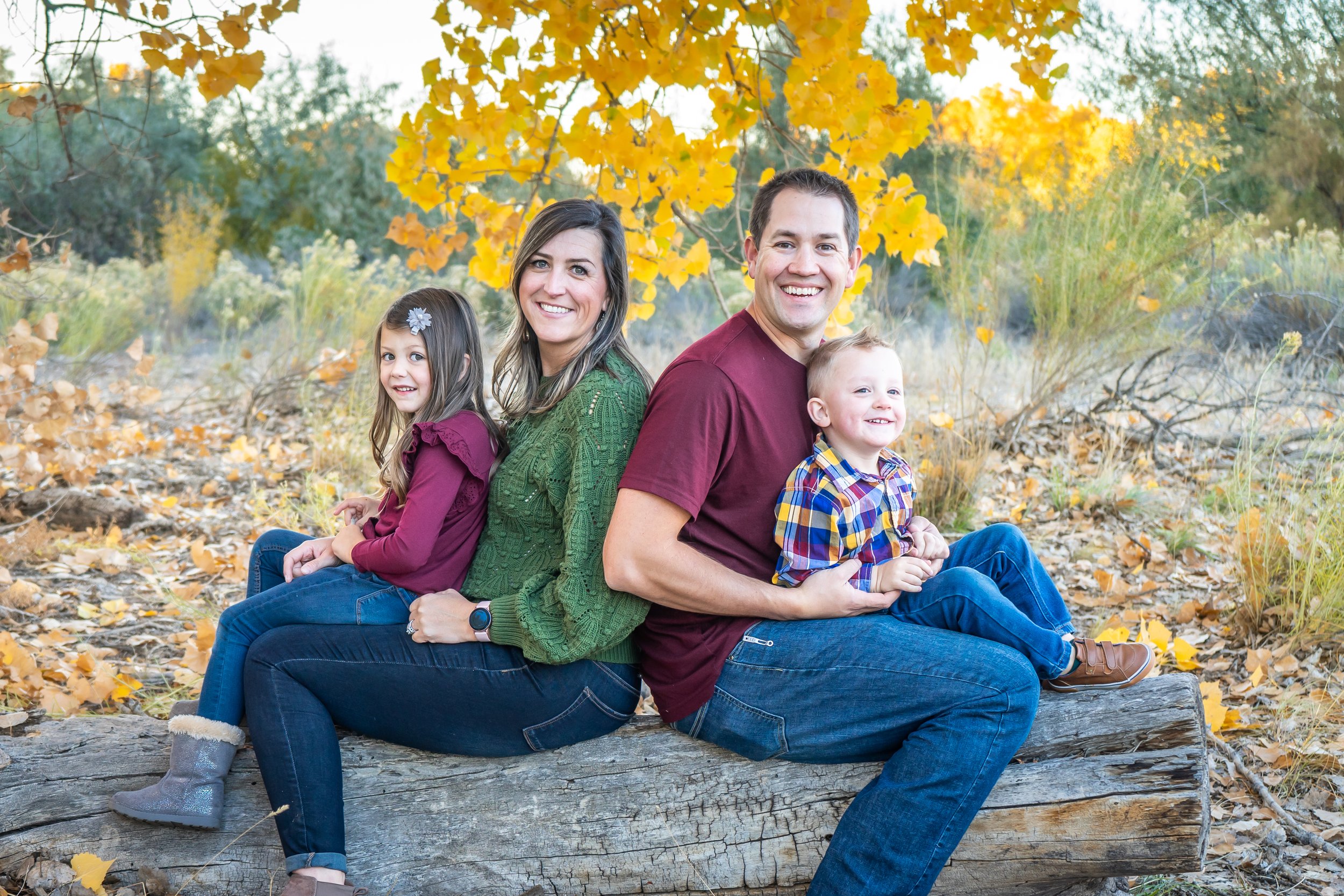 Megan and Craig sit on a log with their 2 young children with the fall leaves behind them