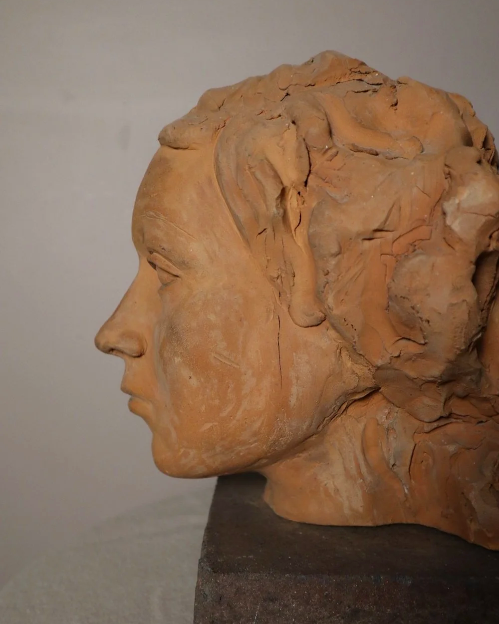 A signed, 20th century art studio terracotta female bust with stone display plinth.