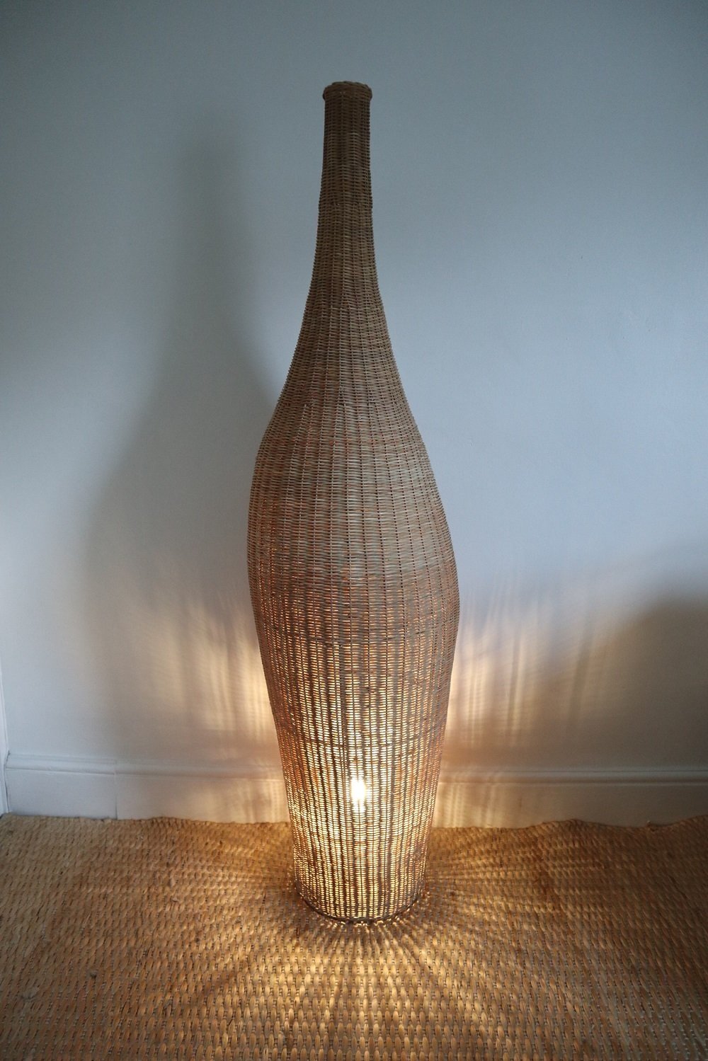 Vintage sculptural woven wicker Bolla floor lamp in the style of Michael Sodeau. Slightly off centred, bottle shaped lamp woven around a black metal frame.