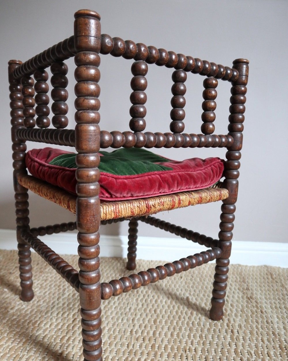 Characterful antique bobbin corner chair with interwoven red and natural rush seat and charming green and red velvet seat cushion. Circa 19th Century.