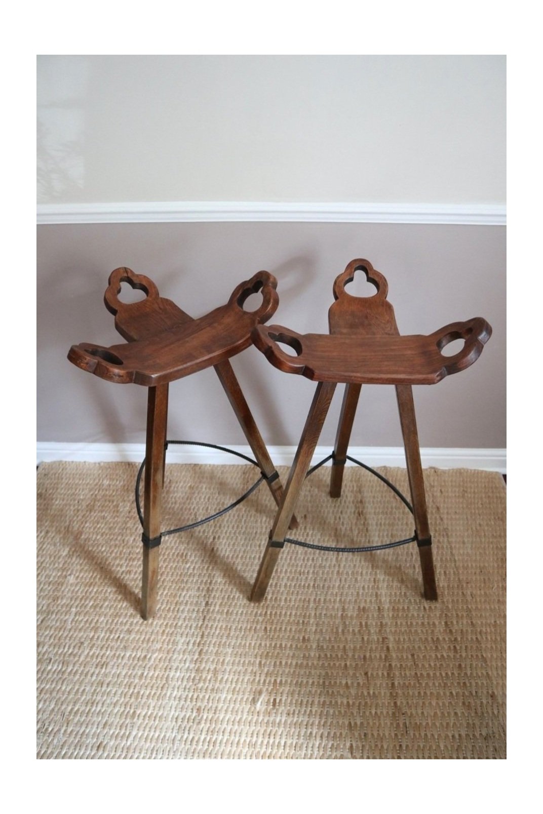 Pair of 1970s Brutalist Spanish style wooden tripod bar stools with hammered iron footrests and curved, carved seats.