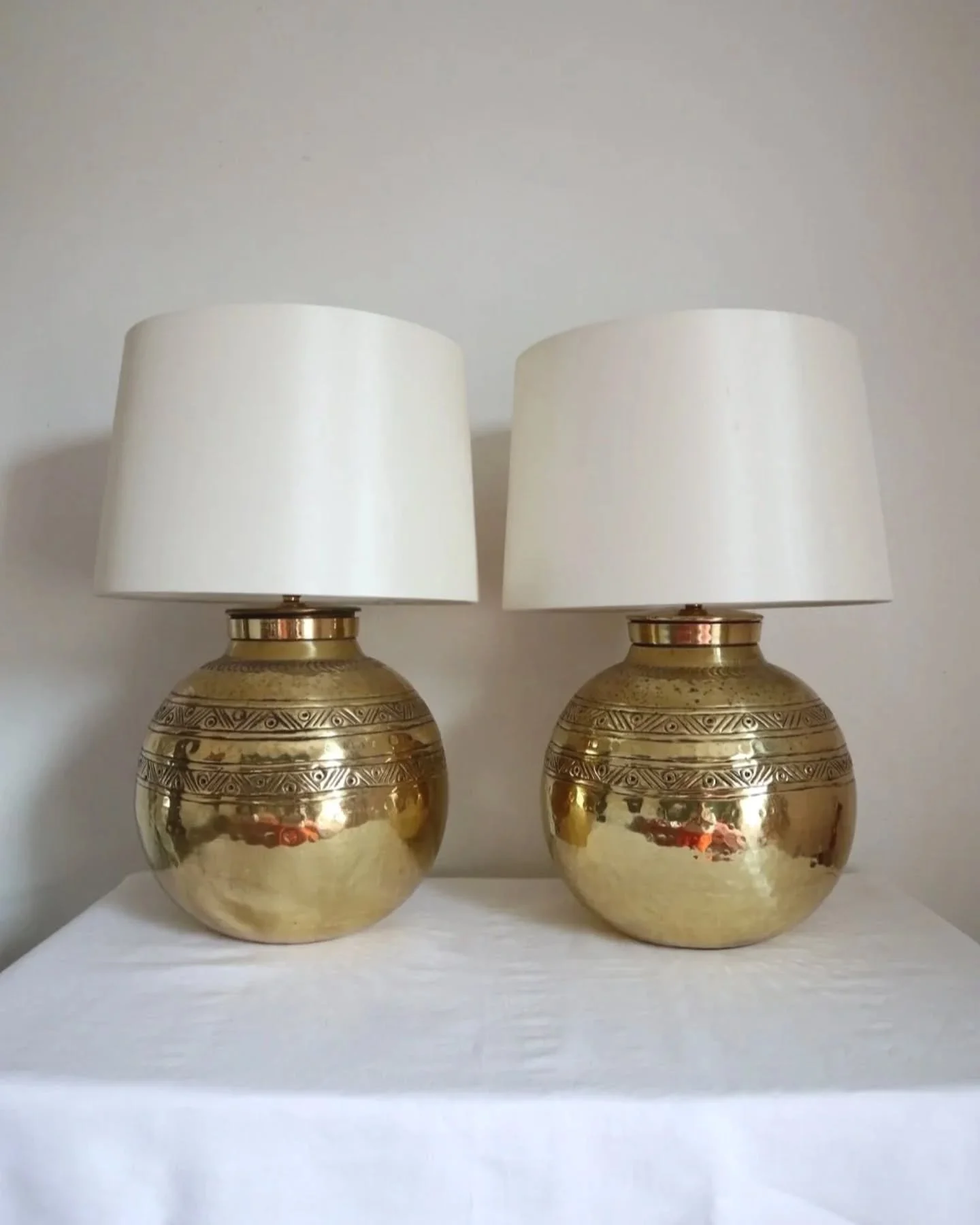 Available online ~  Pair of large, vintage beaten brass spherical table lamps with etched decoration. 

Come with new, white silk slightly tapered lampshades. 

Rewired and PAT tested. 

In good vintage condition with visible tarnishing and some ligh
