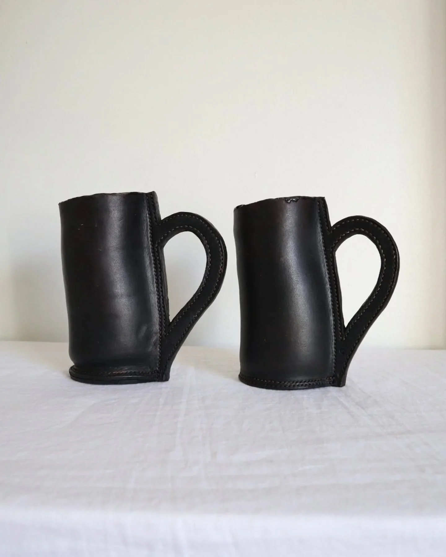 Available online ~ Pair of vintage black leather sculptural tankards with stitched handles.

Medieval style blackjack mugs made with real leather and lined with an epoxy resin for waterproofing. Age unknown, but likely to be more recent replicas. 

B