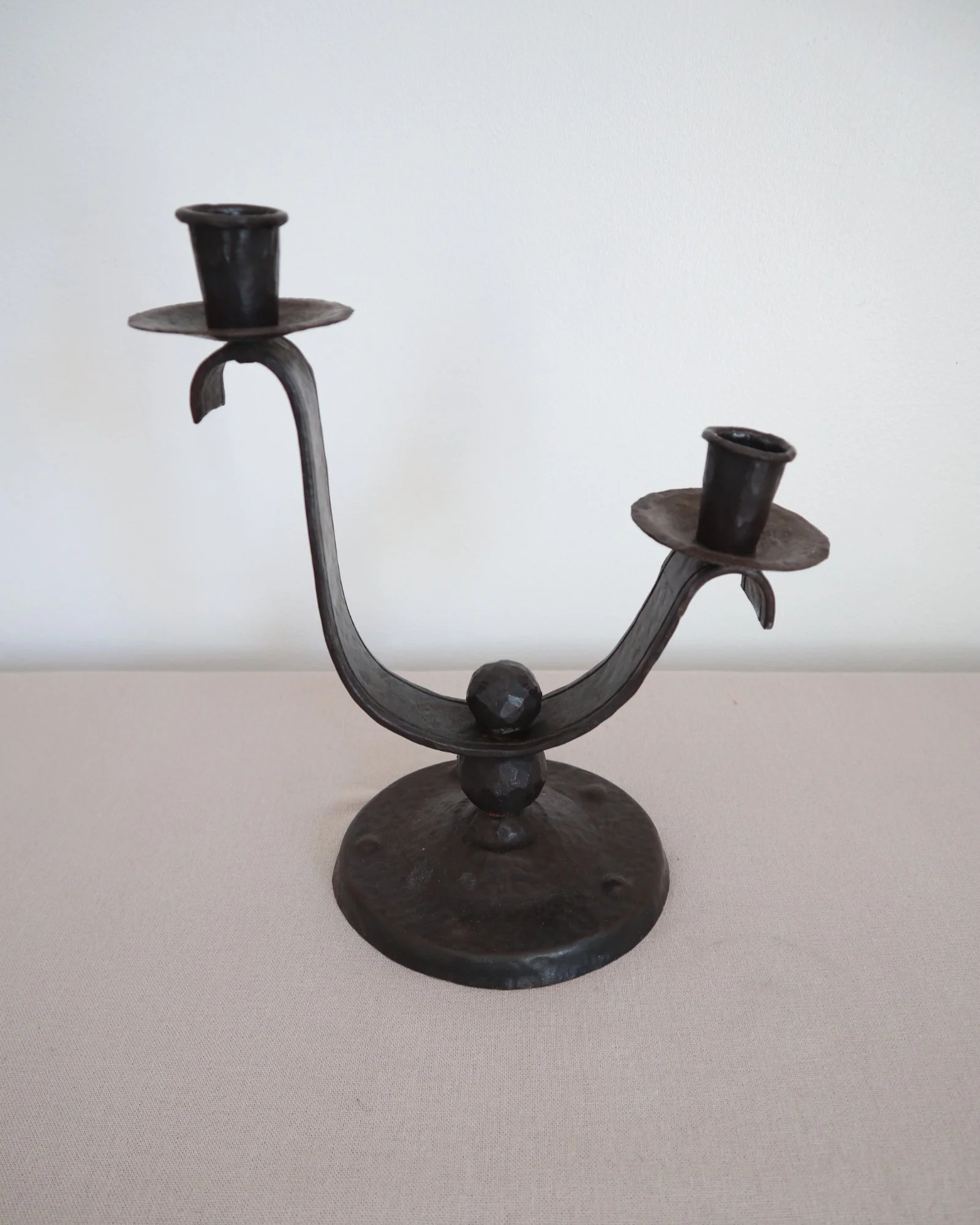 Heavy Brutalist style forged iron candleholder with off set double arms and circular base.