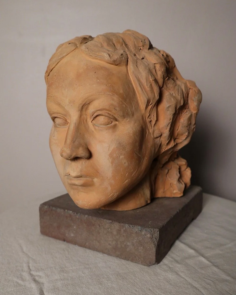 A signed, 20th century art studio terracotta female bust with stone display plinth.