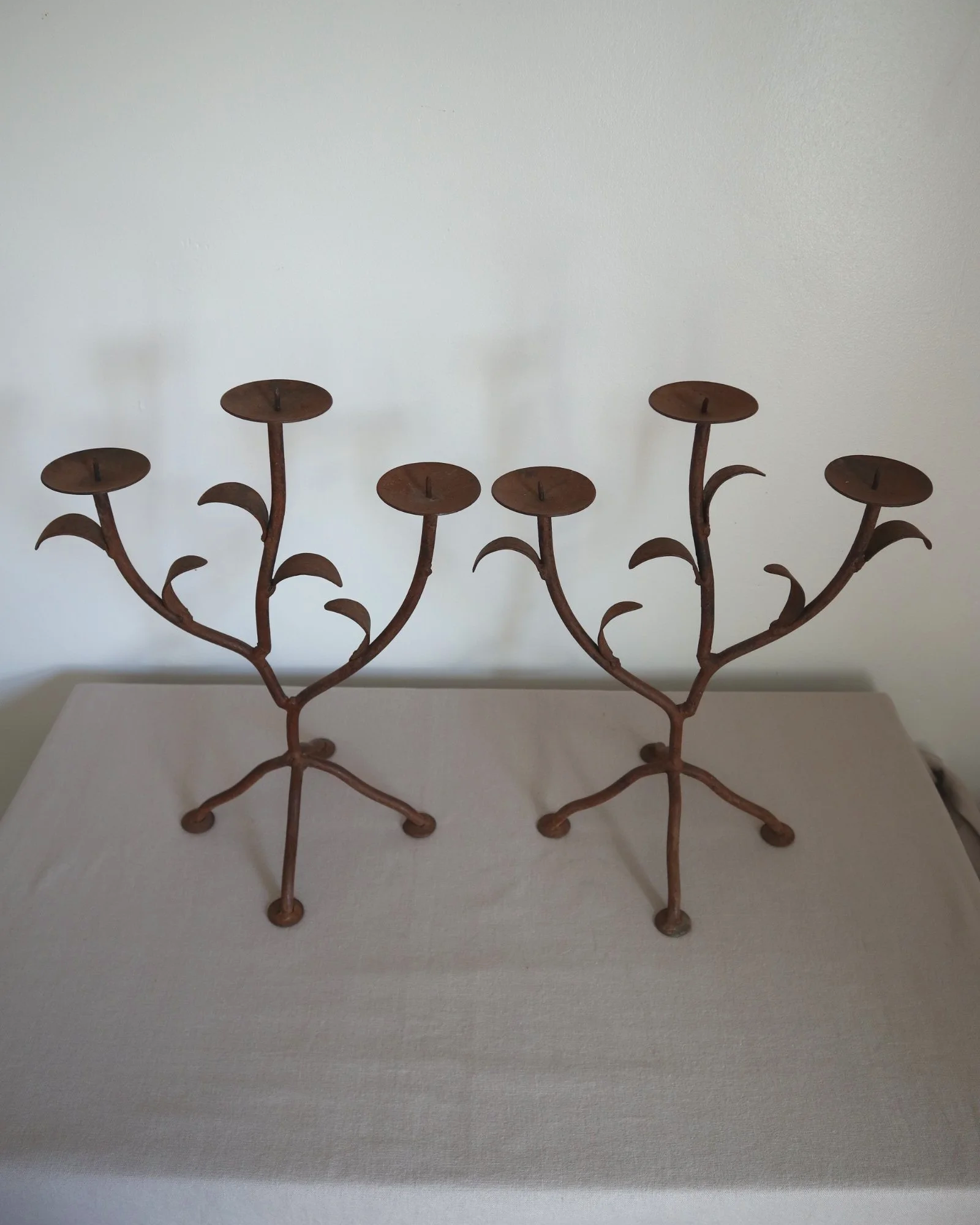 Pair of mid-century, sculptural hand crafted wrought iron 3-arm candle holders with decorative leaves and four footed base.