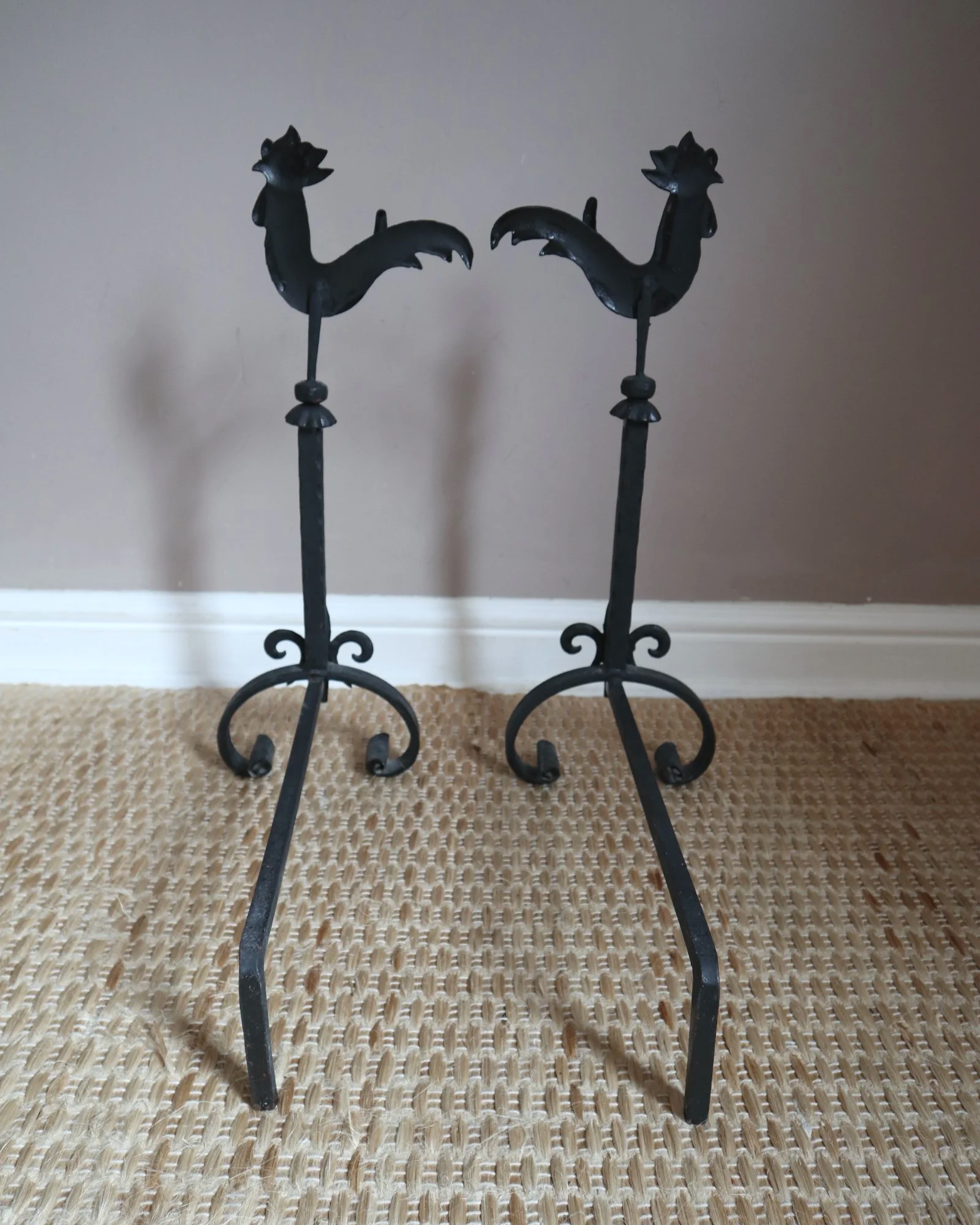Pair of black wrought-iron andirons or firedogs featuring stylized rooster finials, circa mid-20th century.