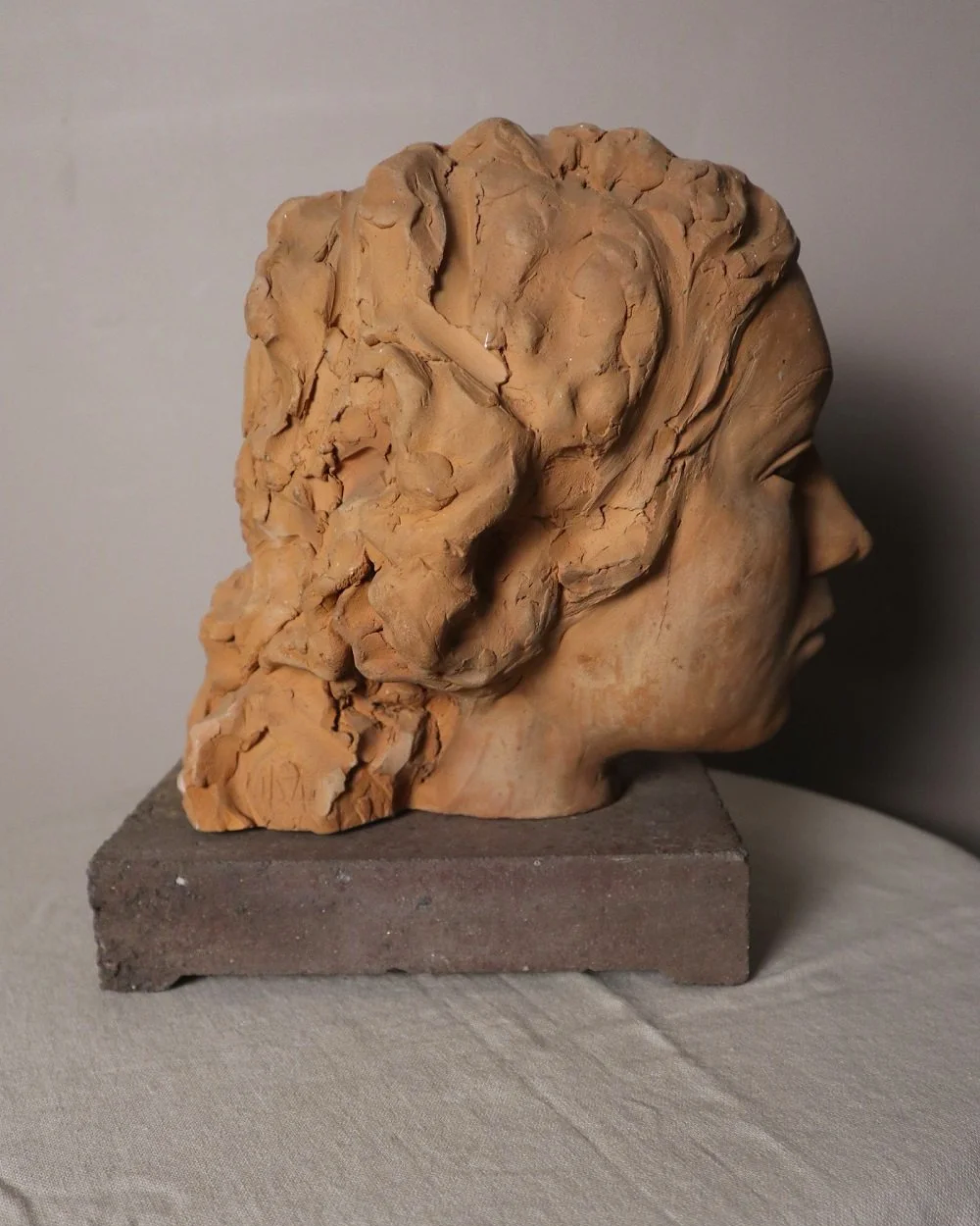 A signed, 20th century art studio terracotta female bust with stone display plinth.