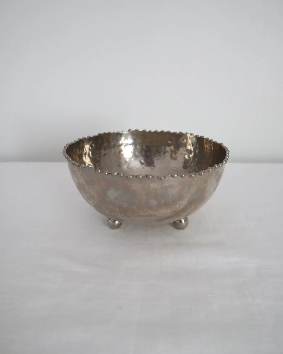 Small hammered metal lightweight circular dish with three ball feet and decorative beaded edging.