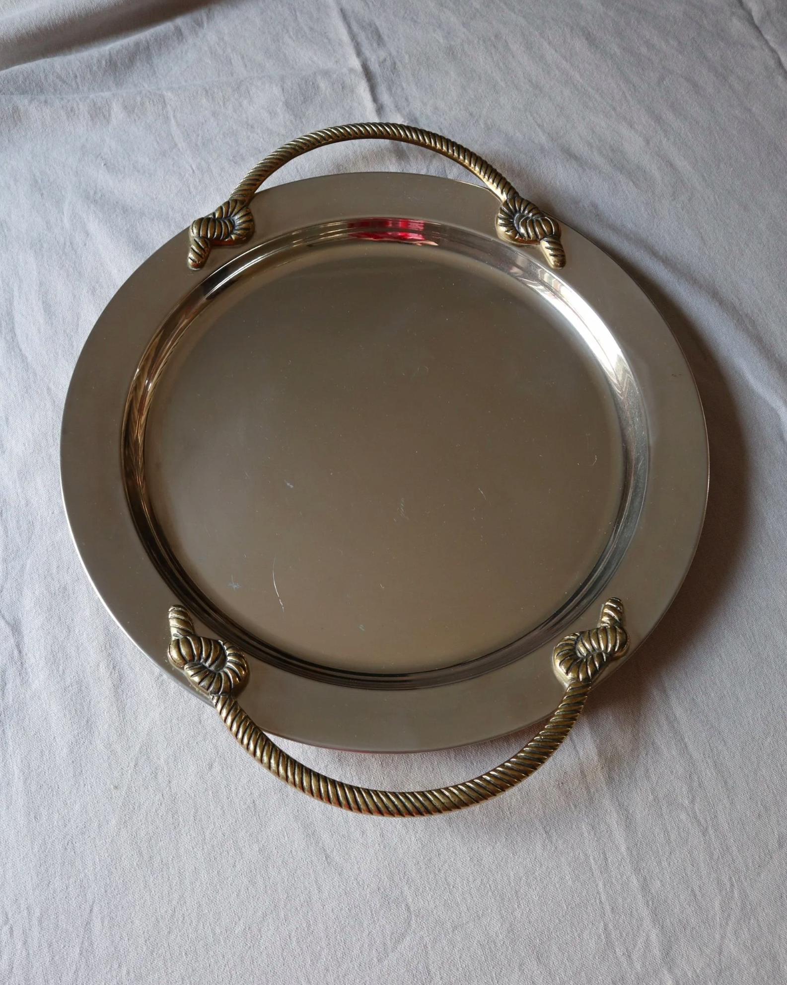 Large mid century circular shiny metal serving tray with elegant brass rope design handles.