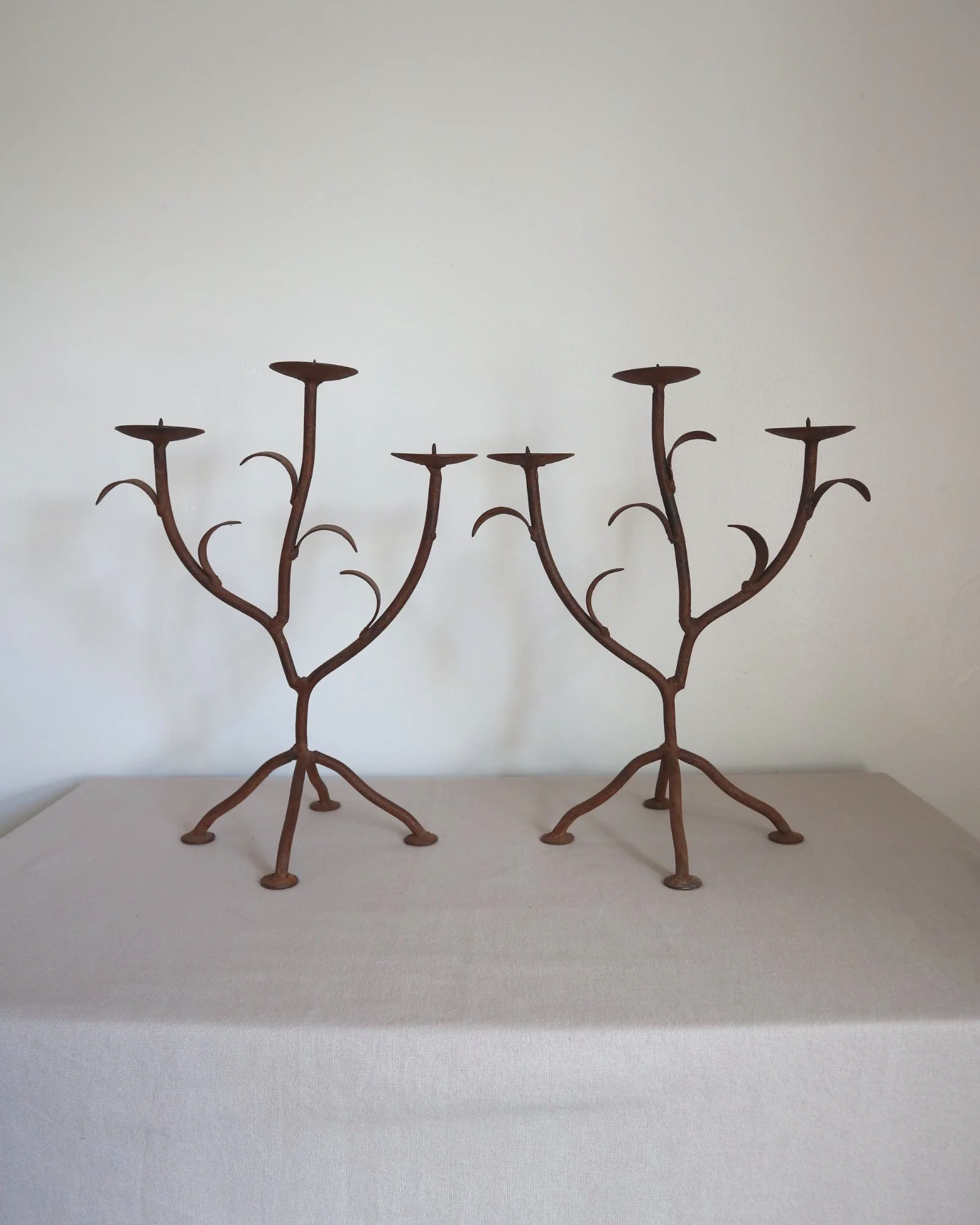 Pair of mid-century, sculptural hand crafted wrought iron 3-arm candle holders with decorative leaves and four footed base.
