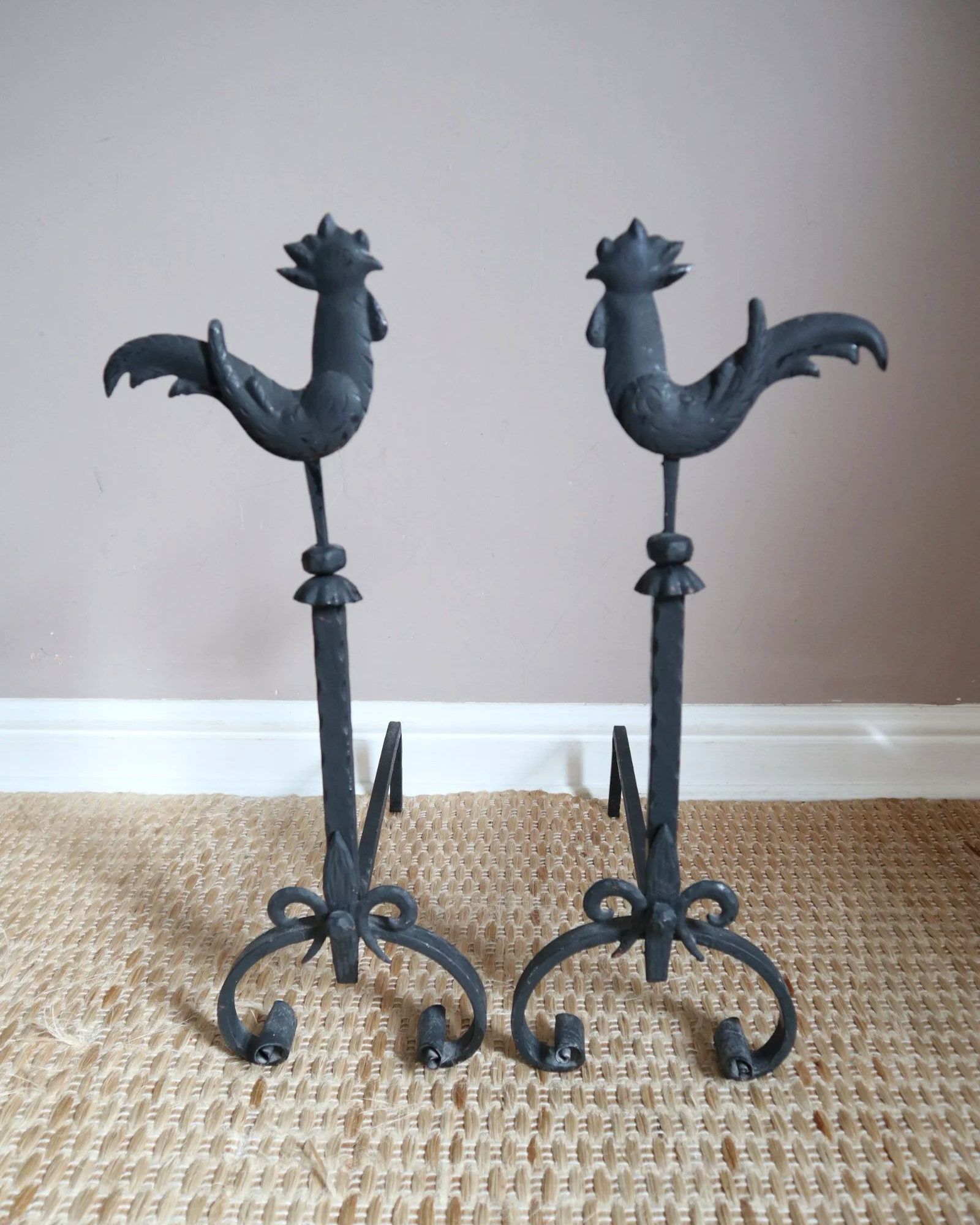 Pair of black wrought-iron andirons or firedogs featuring stylized rooster finials, circa mid-20th century.