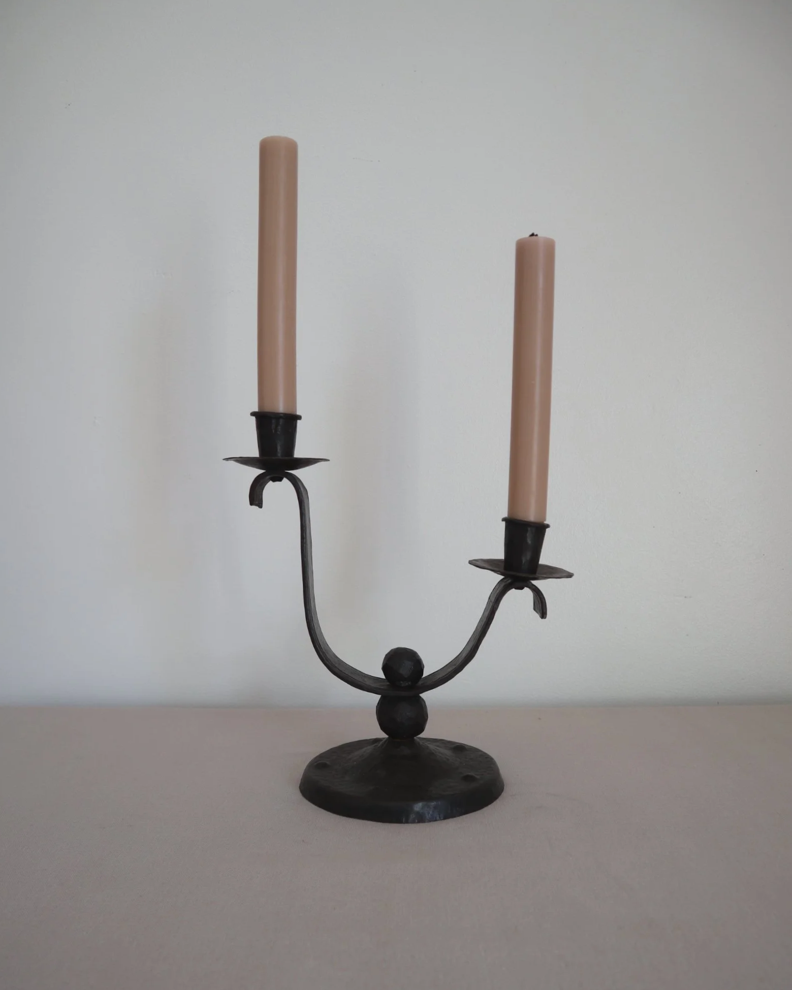 Heavy Brutalist style forged iron candleholder with off set double arms and circular base.