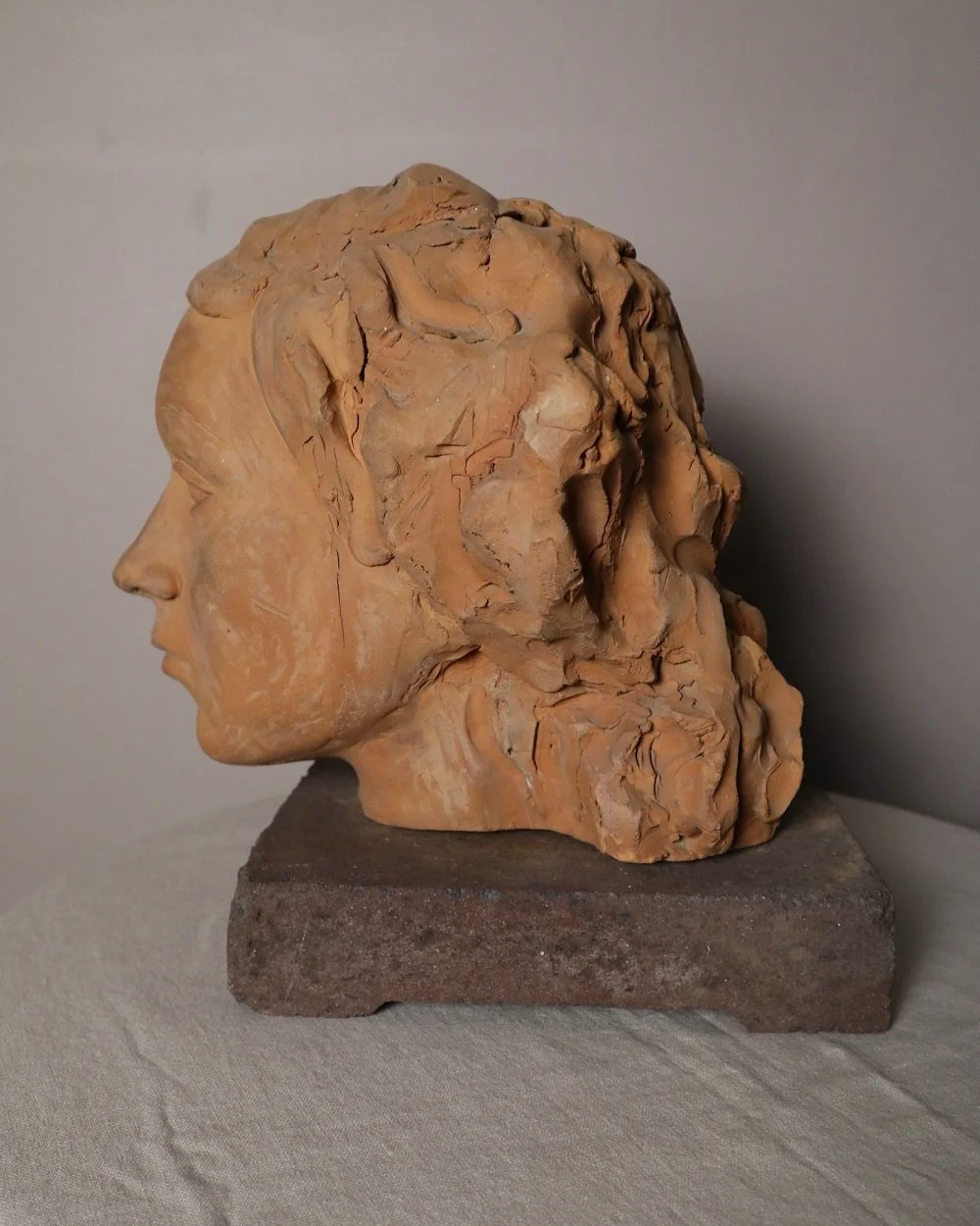 A signed, 20th century art studio terracotta female bust with stone display plinth.