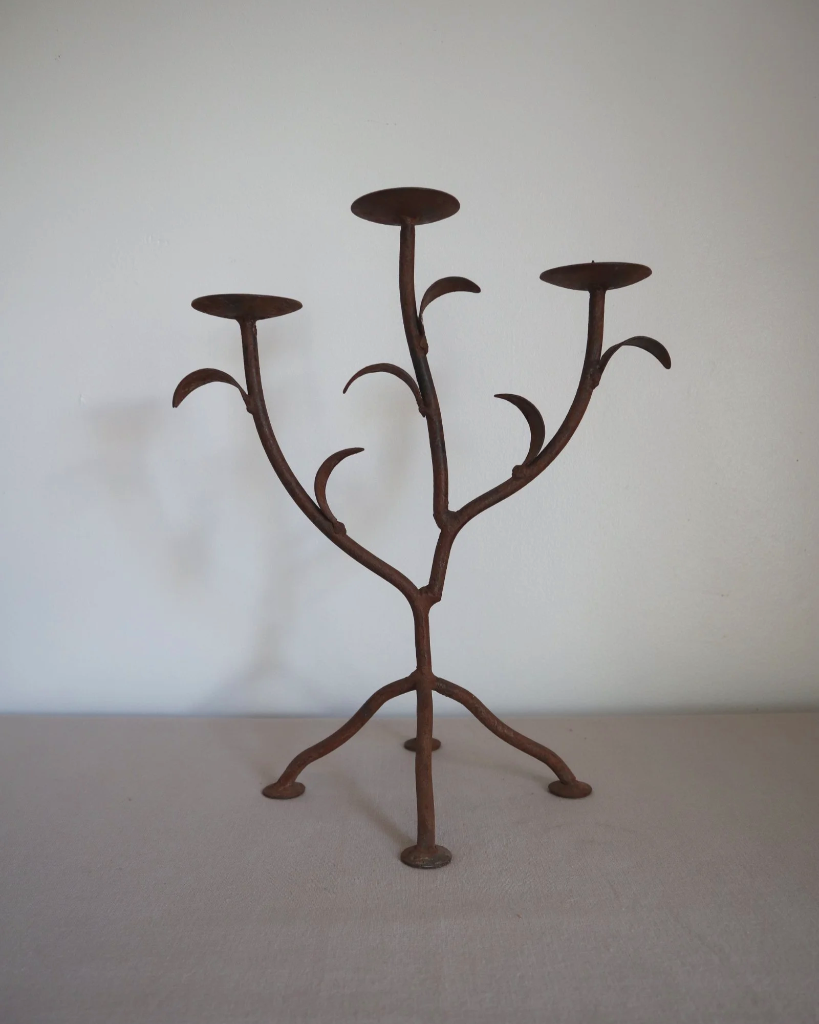 Pair of mid-century, sculptural hand crafted wrought iron 3-arm candle holders with decorative leaves and four footed base.