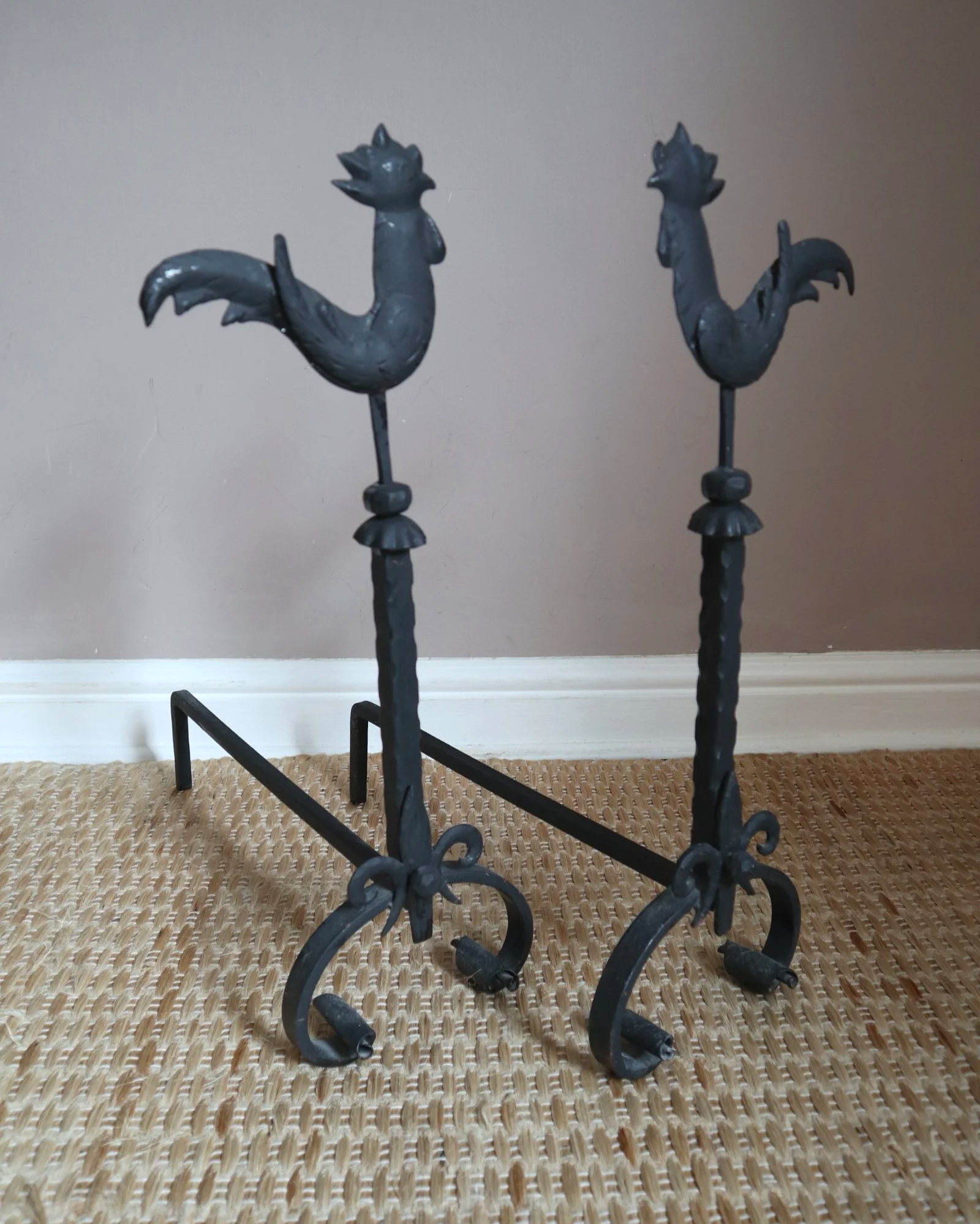 Pair of black wrought-iron andirons or firedogs featuring stylized rooster finials, circa mid-20th century.