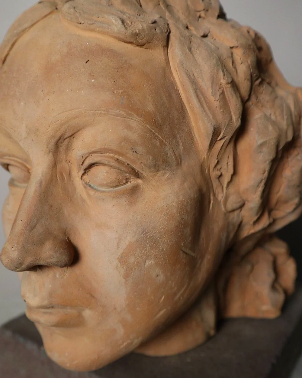 A signed, 20th century art studio terracotta female bust with stone display plinth.