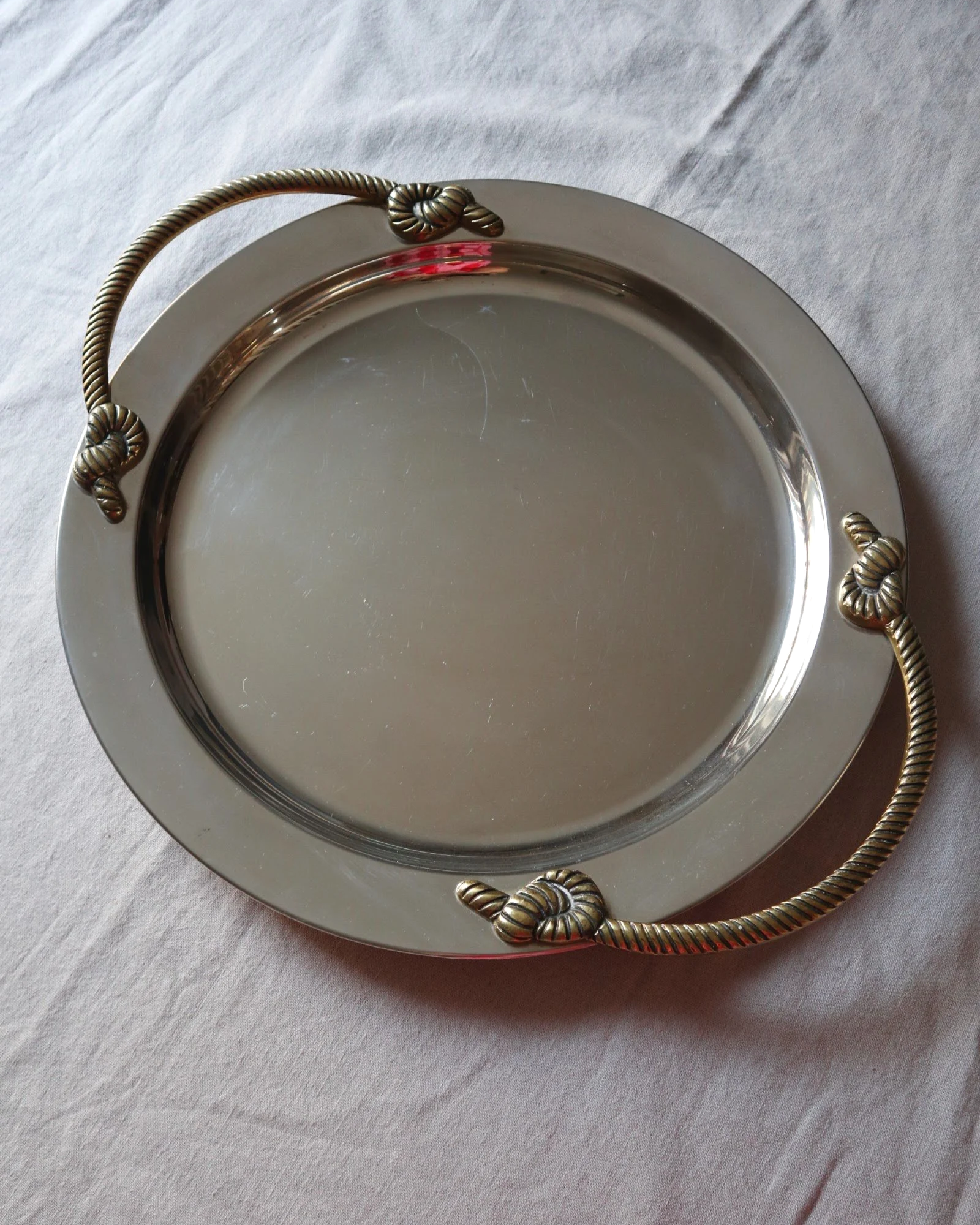 Large mid century circular shiny metal serving tray with elegant brass rope design handles.