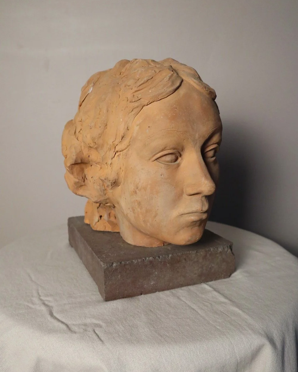 A signed, 20th century art studio terracotta female bust with stone display plinth.