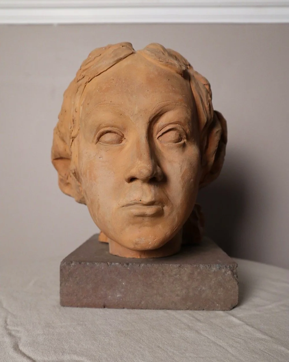 A signed, 20th century art studio terracotta female bust with stone display plinth.