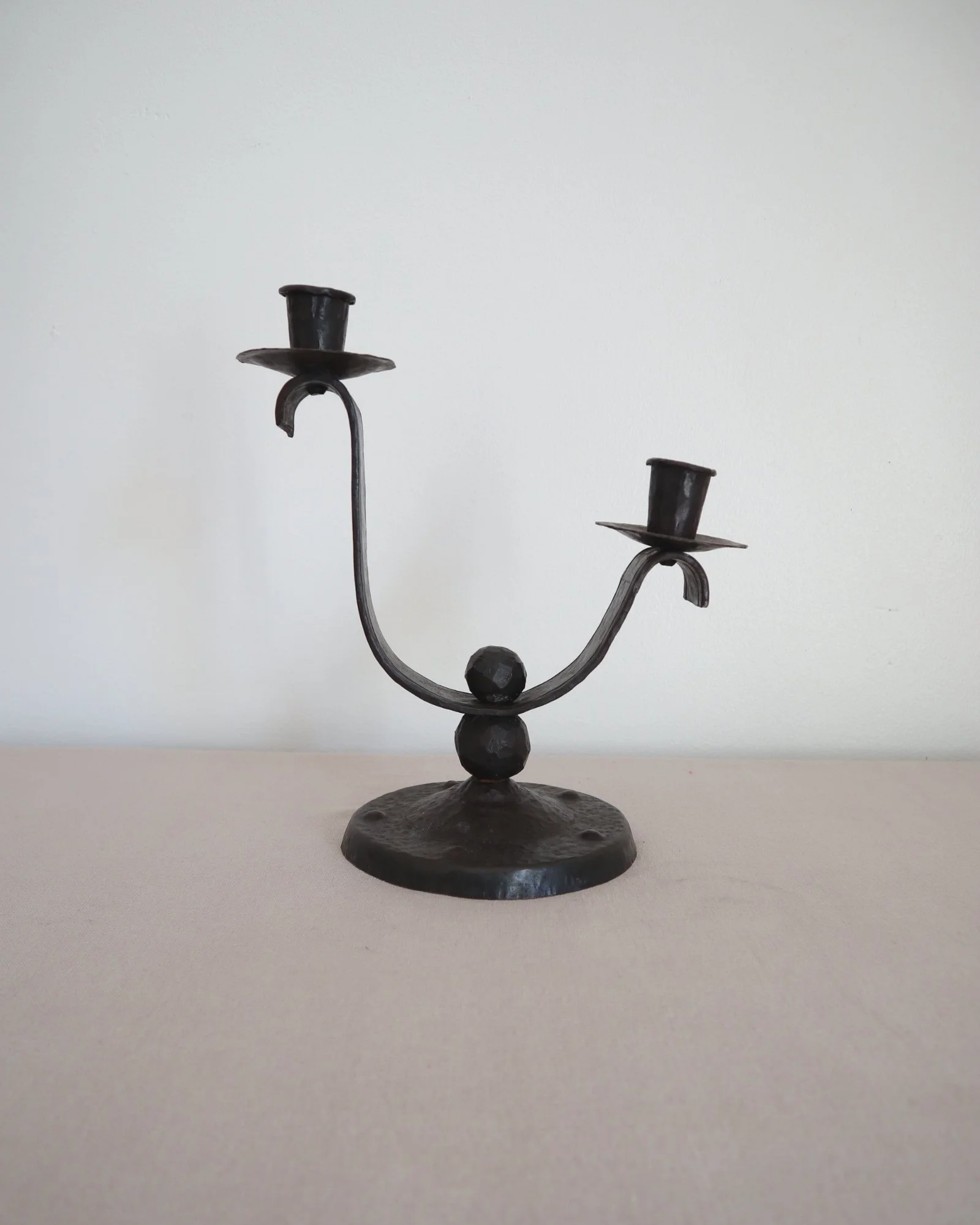 Heavy Brutalist style forged iron candleholder with off set double arms and circular base.