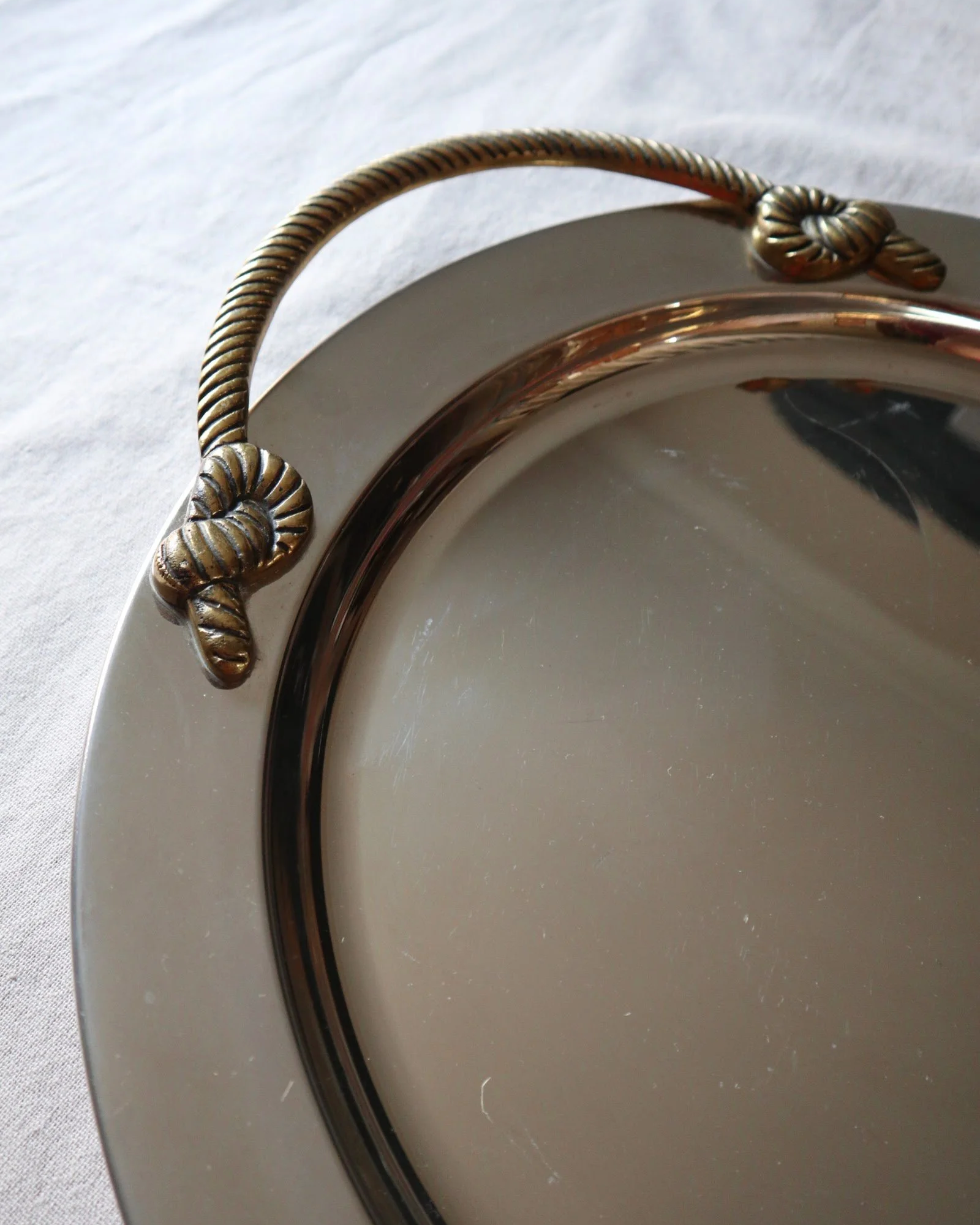 Large mid century circular shiny metal serving tray with elegant brass rope design handles.