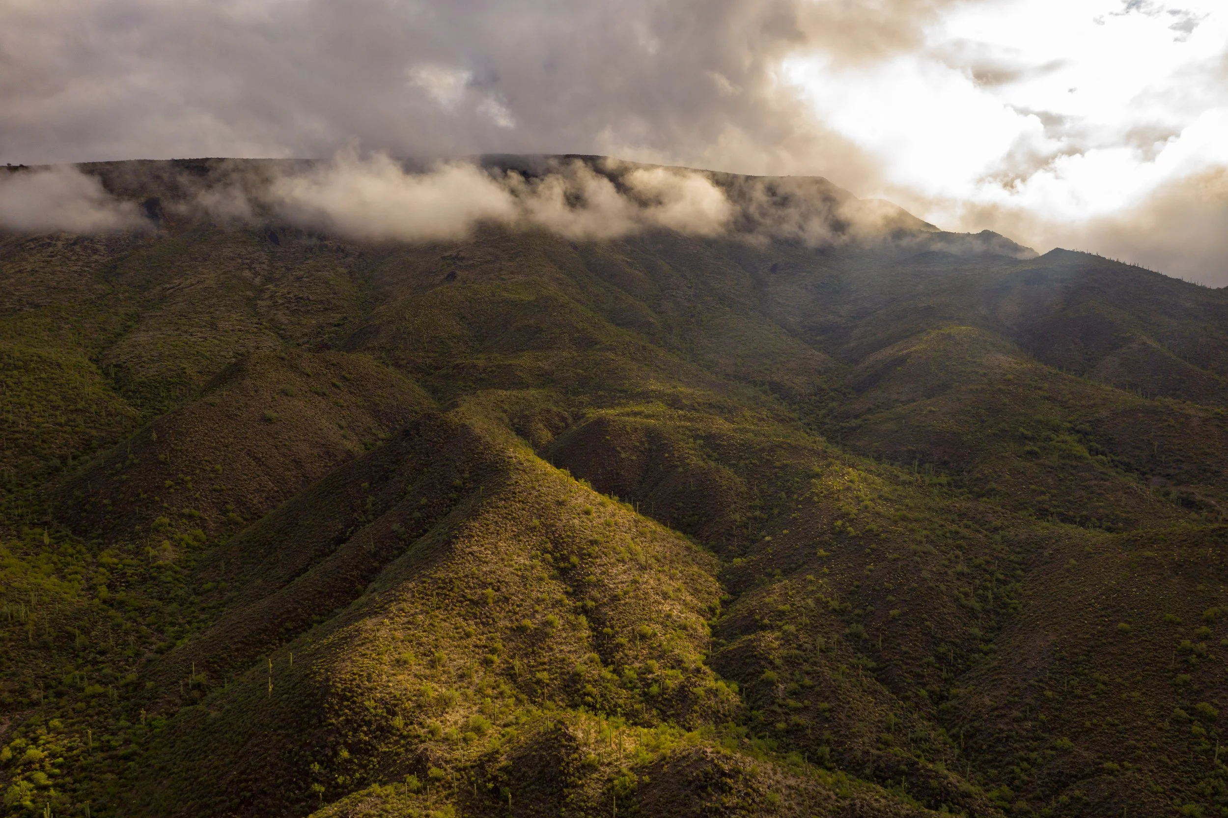 A mountain landscape with green vegetation on the slopes and clouds and mist surrounding the peaks.