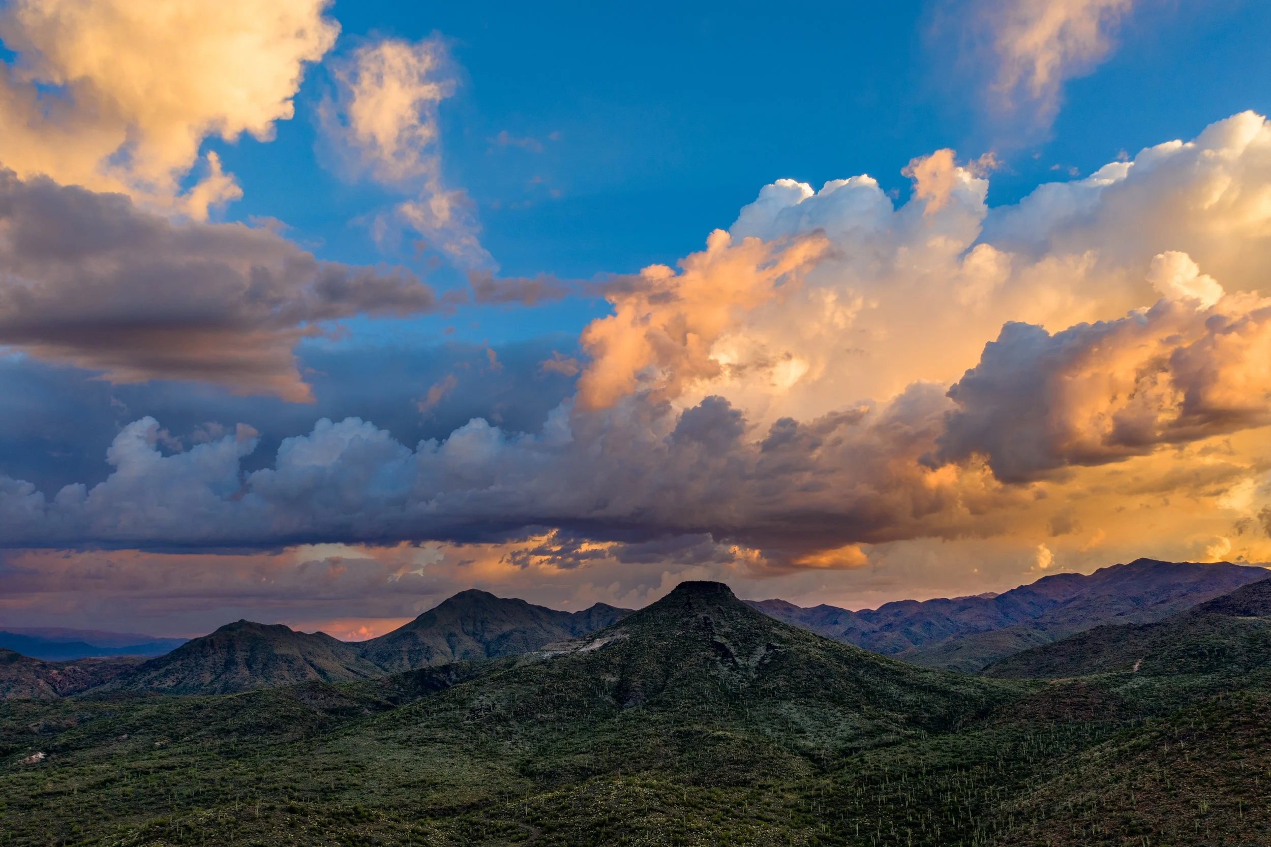 Scenic view of a mountainous landscape under a sky filled with clouds during sunset, with dark mountain silhouettes in the foreground and blue and orange hues in the sky.