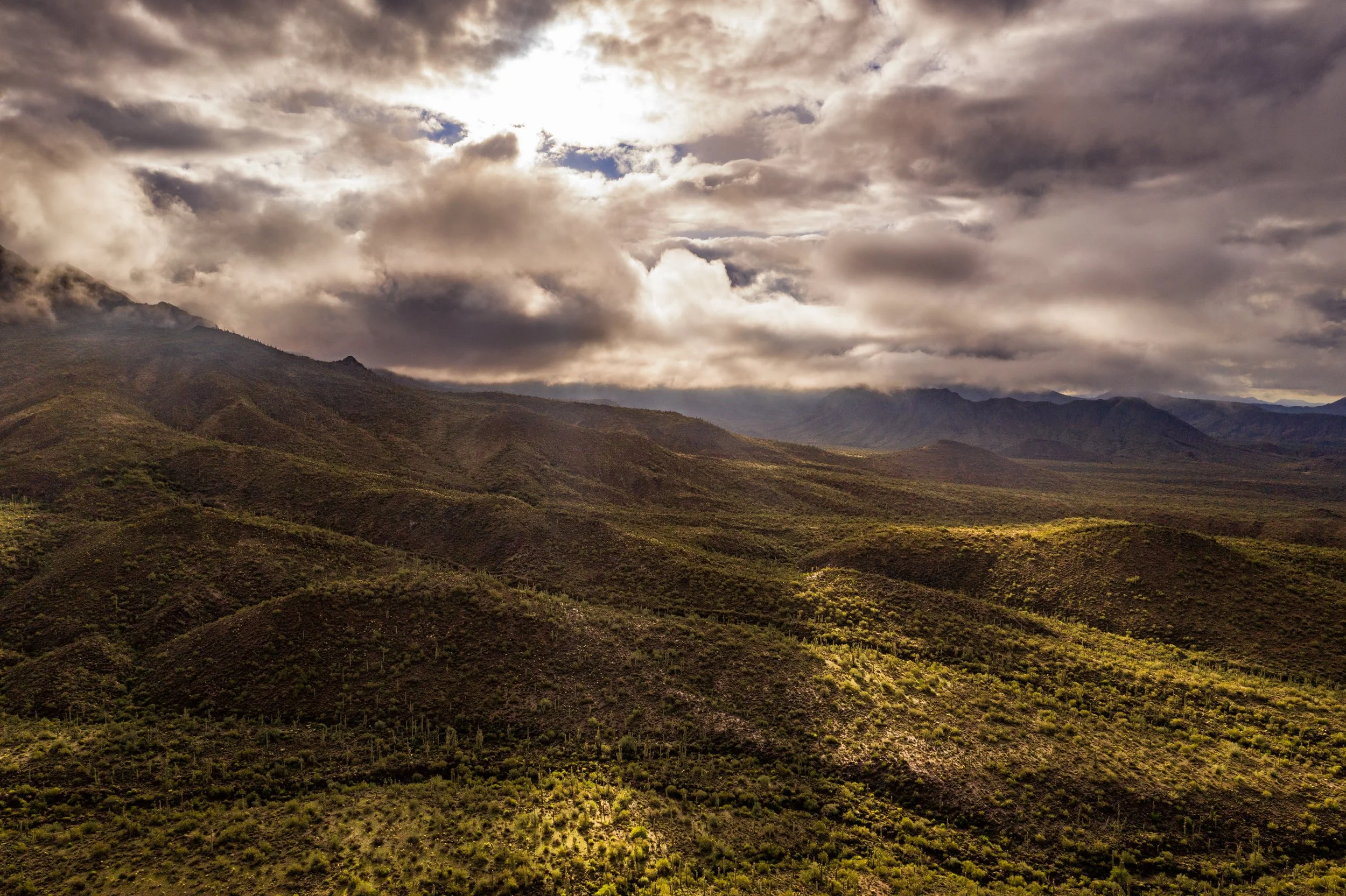 Scenic view of mountains covered with sparse vegetation under a cloudy sky with sunlight breaking through.