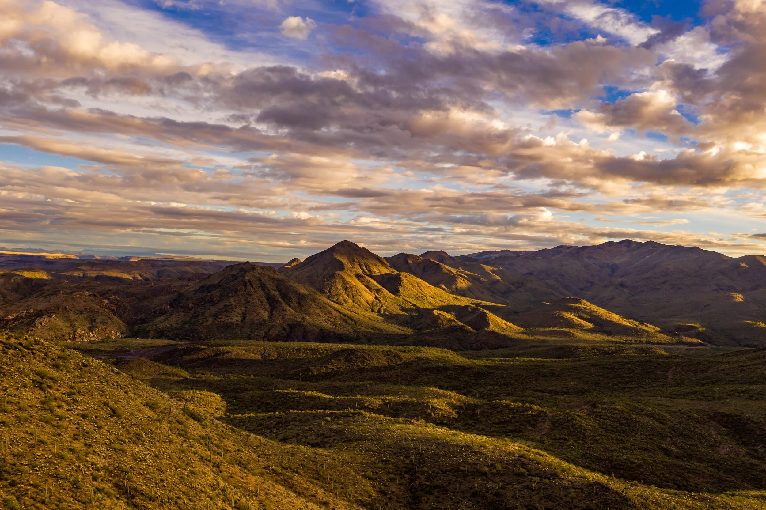 Landscape of rolling green hills and mountains under a partly cloudy sky during sunset.