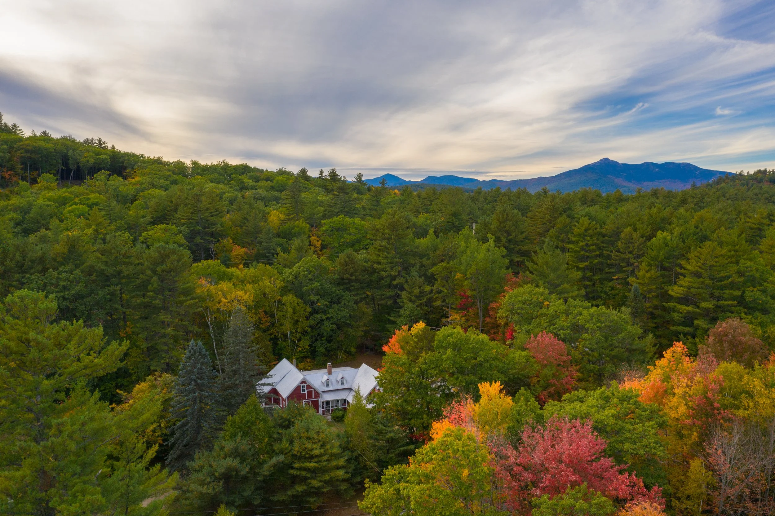 A scenic view of a forested mountain landscape with a house at the bottom, under a sky with some clouds.
