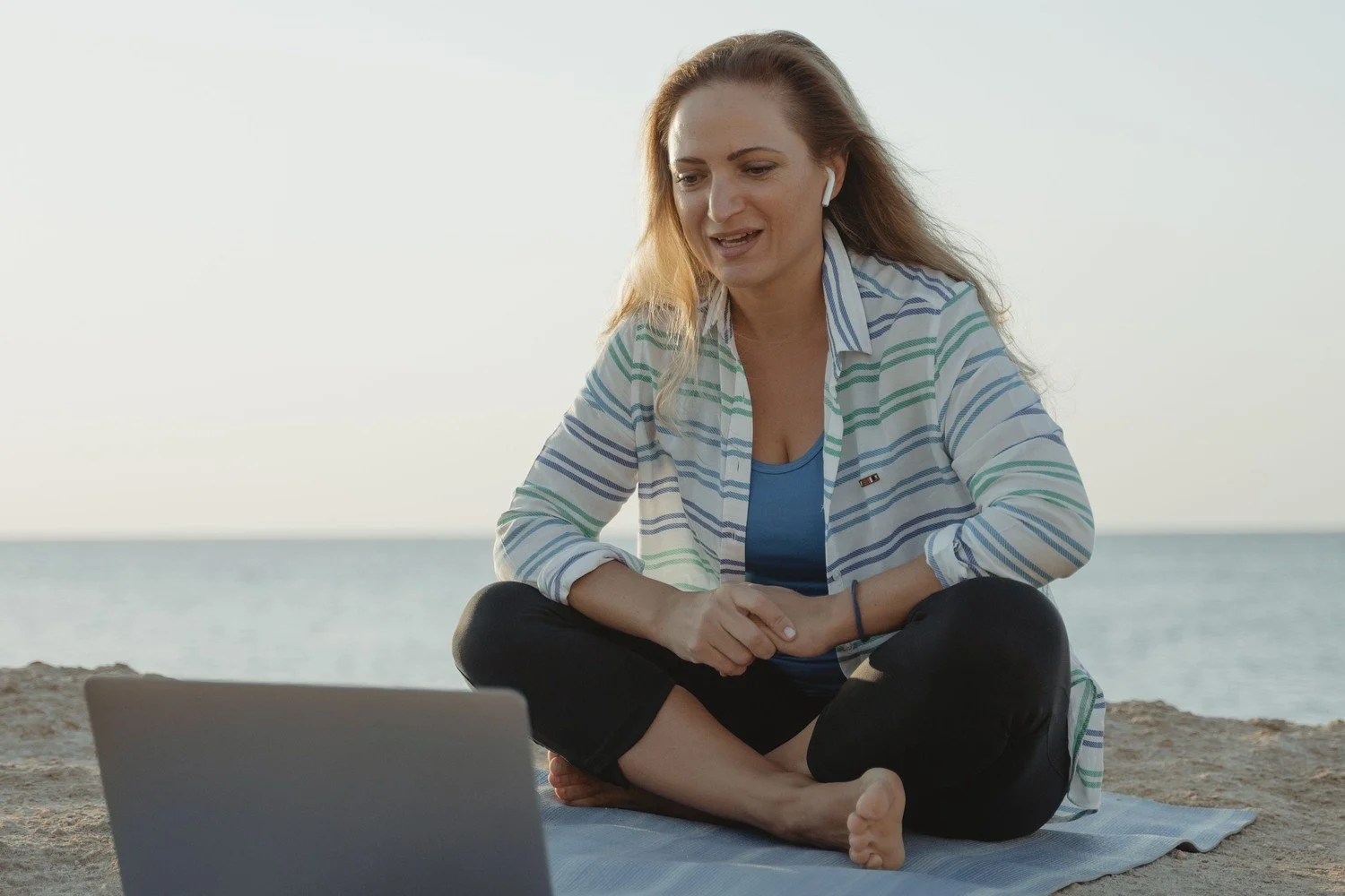 An accounting firm owner sits cross-legged on a mat at the shore at dawn, on a laptop video call, a picture of how tax season burnout follows firm owners even on a break.