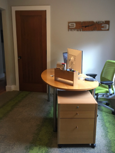 Modern home office with a wooden desk, computer, green swivel chair, and wall-mounted clock.