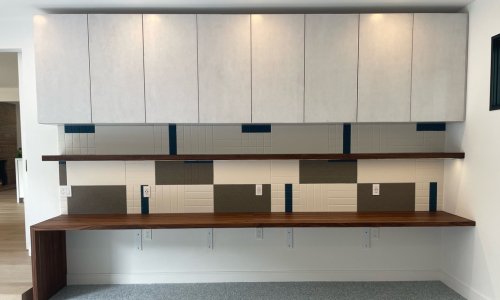 Modern cabinet wall with white upper cabinets, floating shelves, and a wooden countertop featuring diverse tile patterns and electrical outlets.