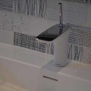 Modern bathroom sink with a sleek chrome faucet and decorative black and white tiled backsplash.