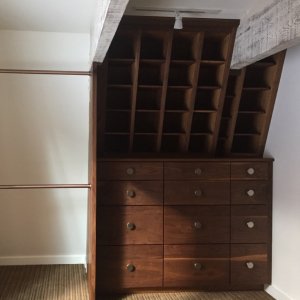 Wooden dresser with multiple drawers and open cubbies in a room with sloped ceiling and carpet flooring.