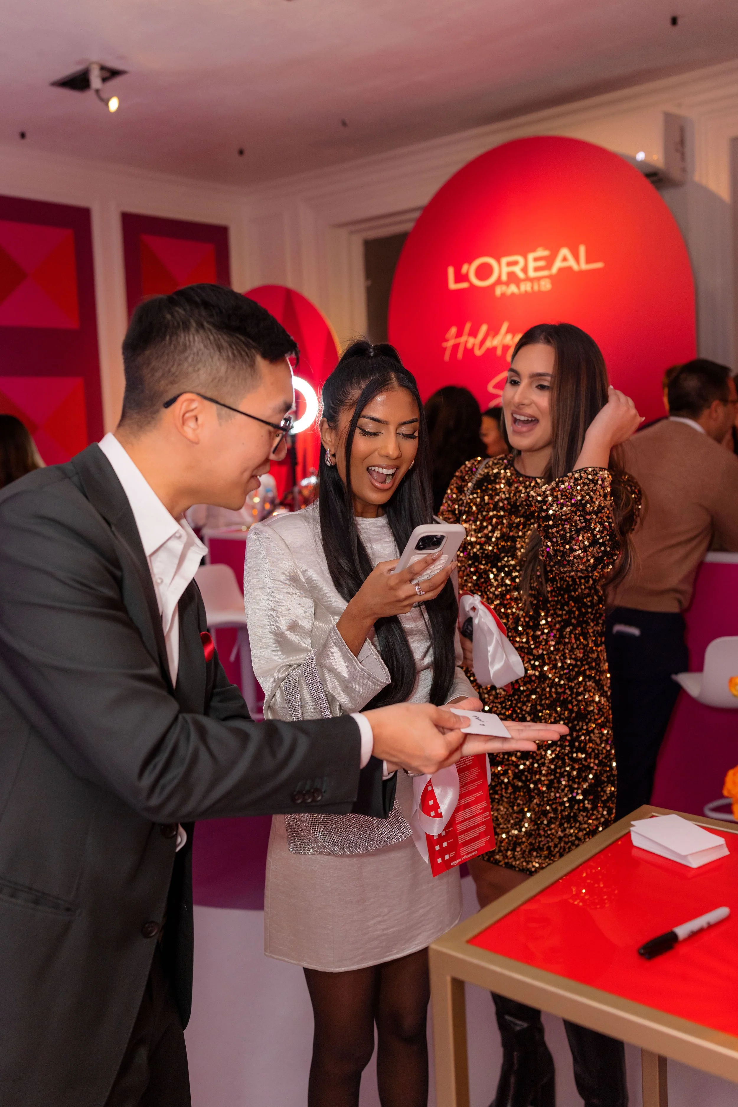 L'Oréal event guests laughing with Montreal magician Bao Magic during a card trick at a festive corporate party.
