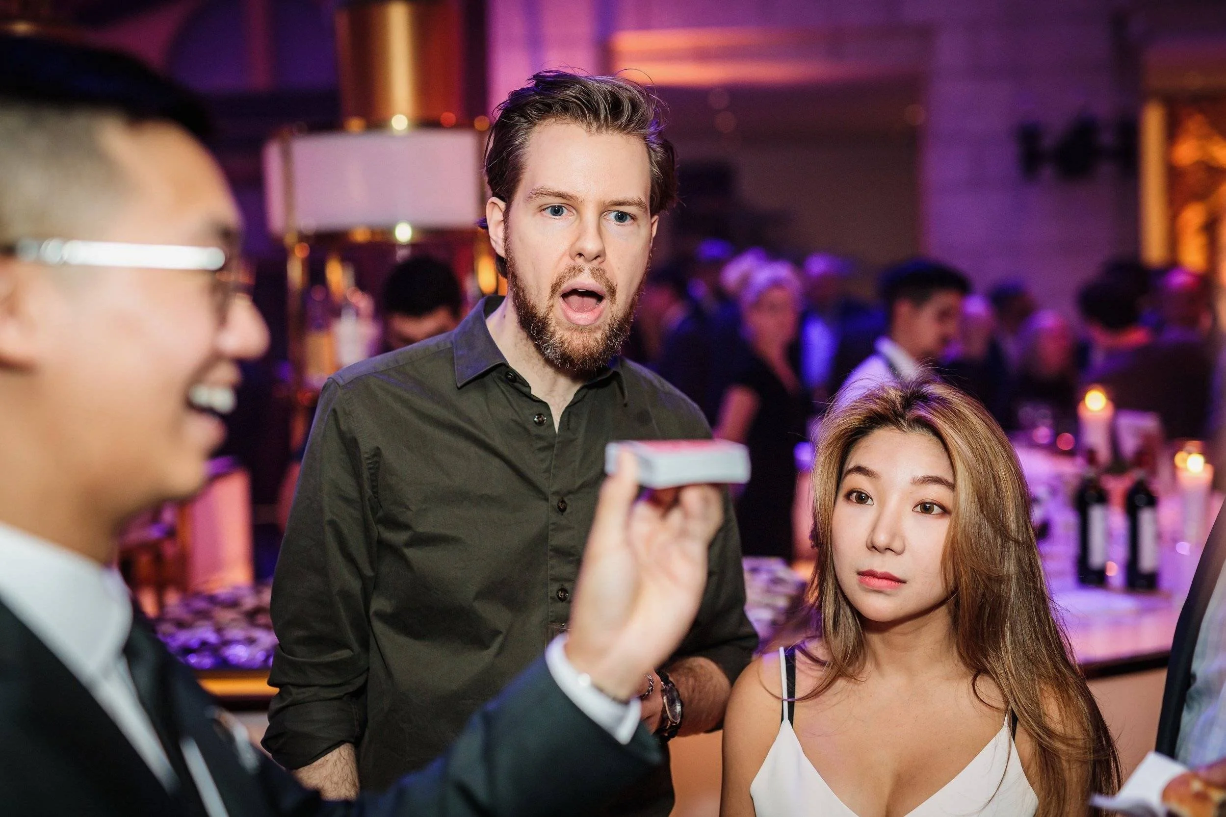 A man stunned by Bao Hoang’s close-up magic at a Montreal corporate event, standing next to a woman in a white dress under vibrant lighting.