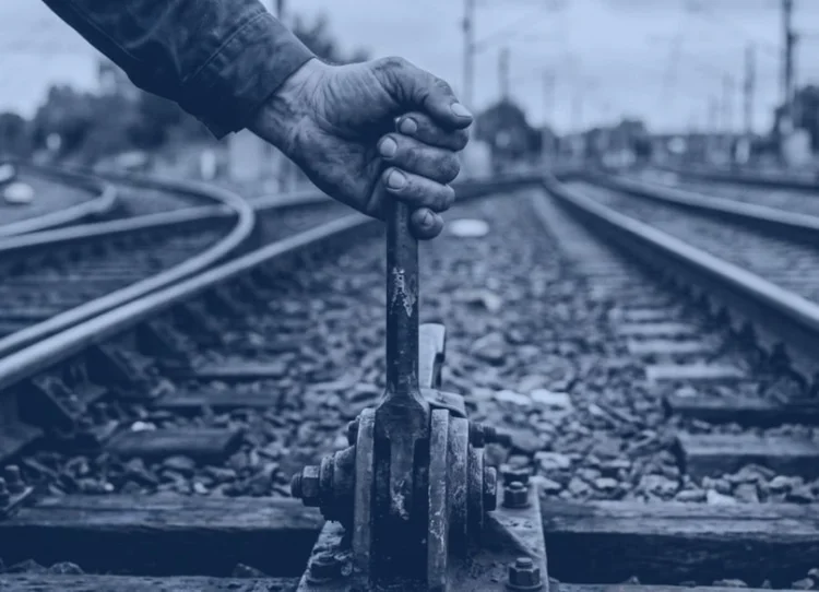 Hand pulling a railway switch lever beside the tracks