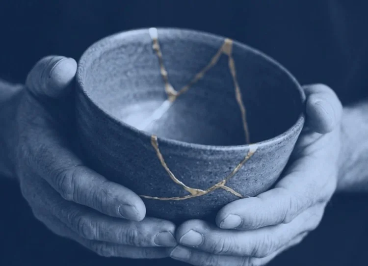 Hands holding a bowl repaired with gold kintsugi seams