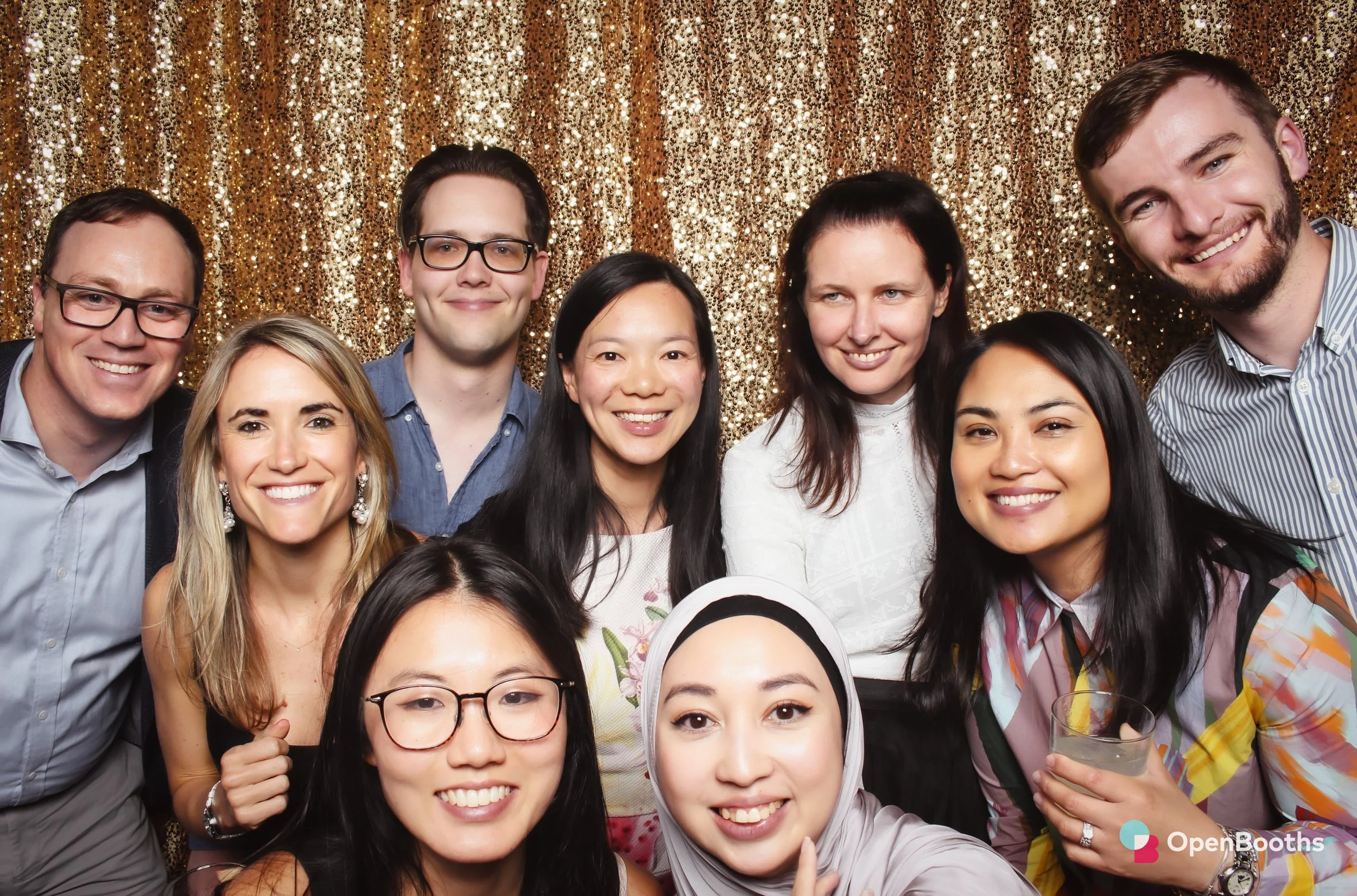A group of people pose in an Open Booths photo booth with a gold sequin backdrop