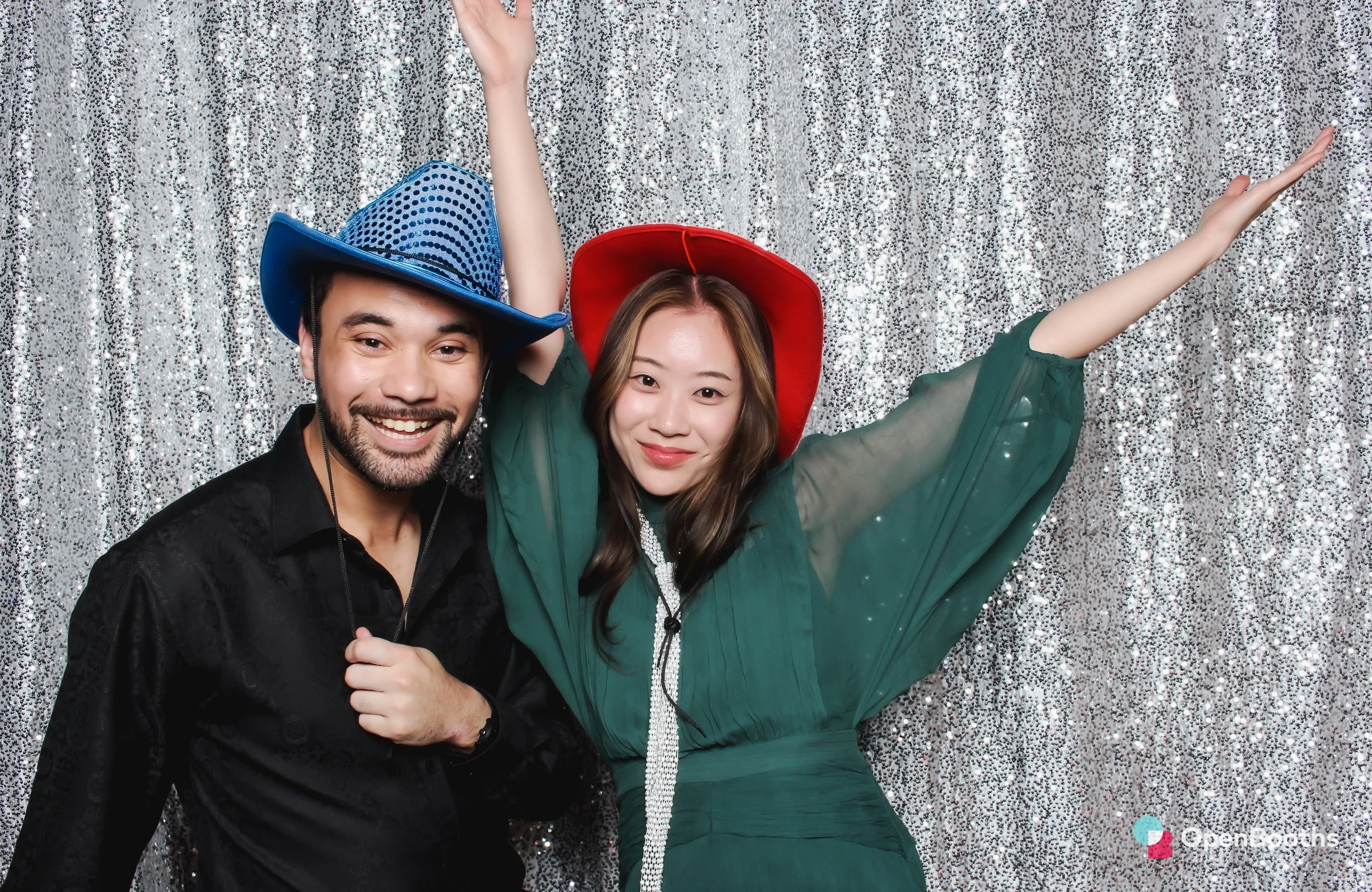 Two people wearing cowboy hats pose in an Open Booths photo booth in front of  a sparkly silver sequin backdrop