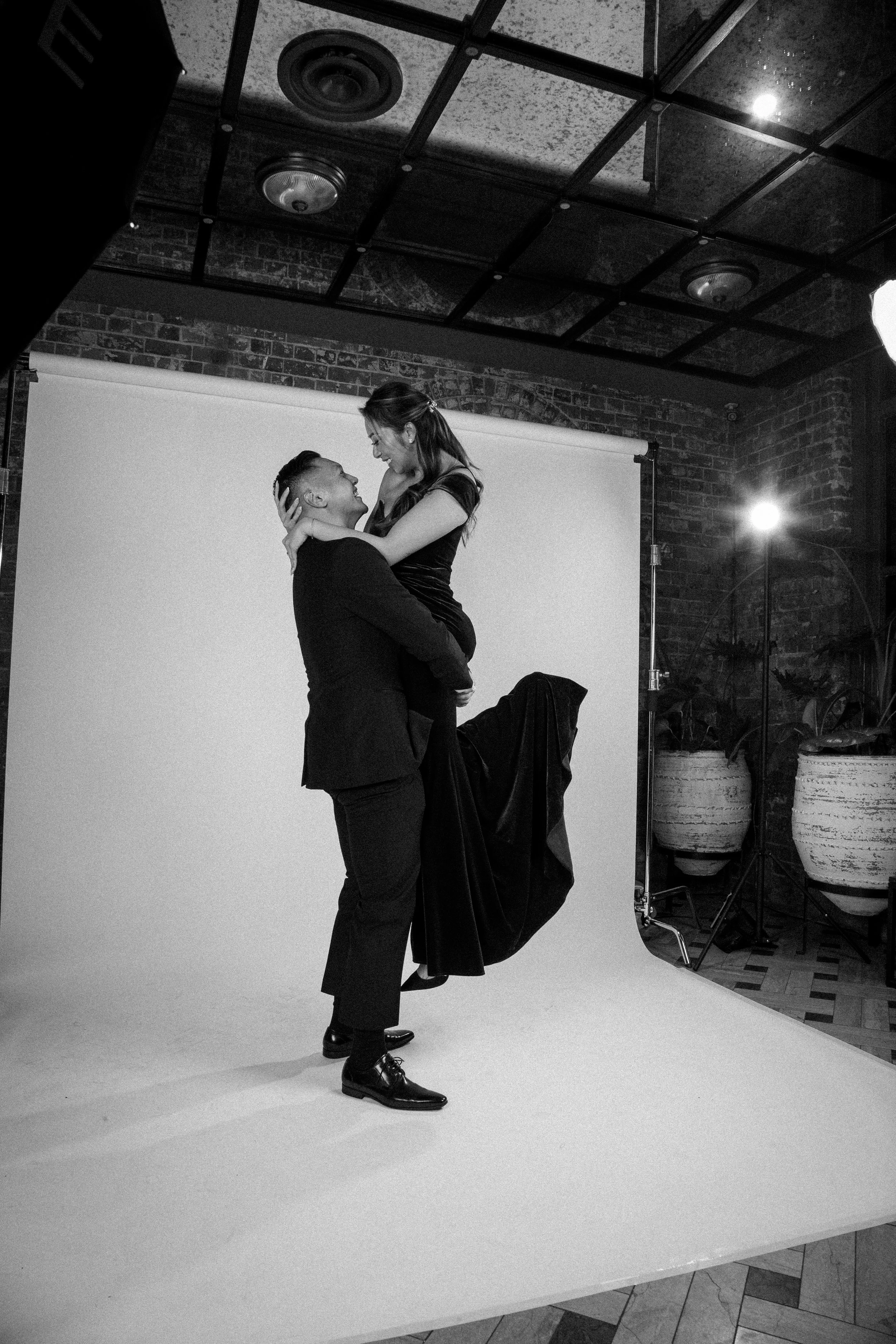 Man lifting a woman playfully in front of a studio backdrop at a formal Sydney wedding celebration.