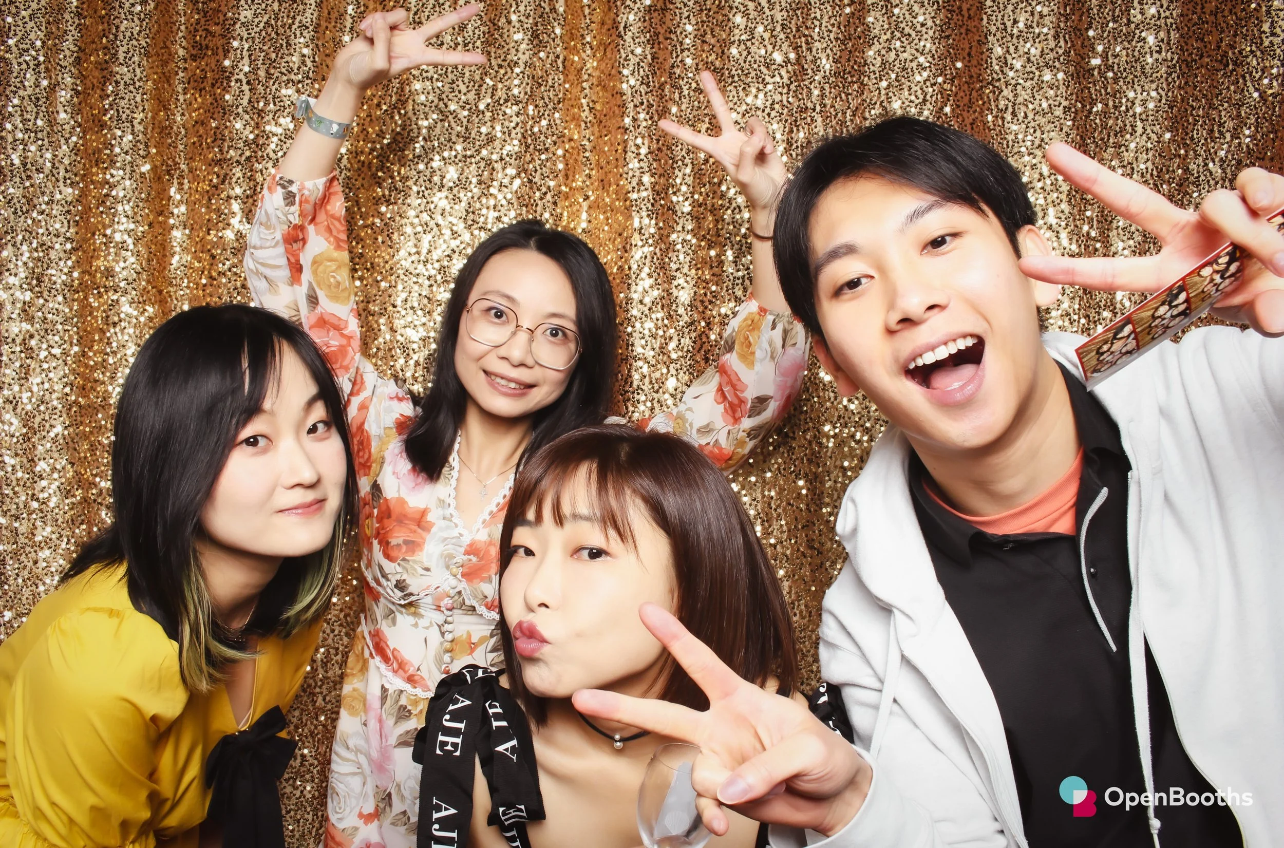 A group of people pose in an Open Booths photo booth with a sparkly gold sequin backdrop