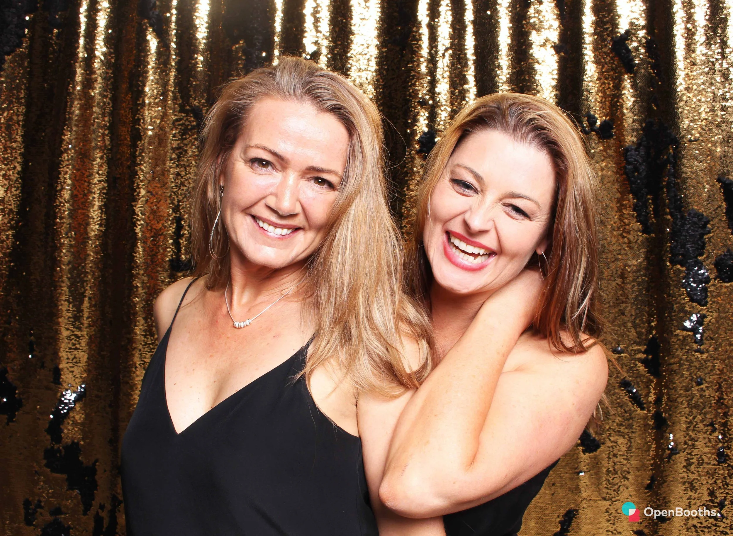 Two people pose in an Open Booths photo booth with a reversible black and gold sequin backdrop