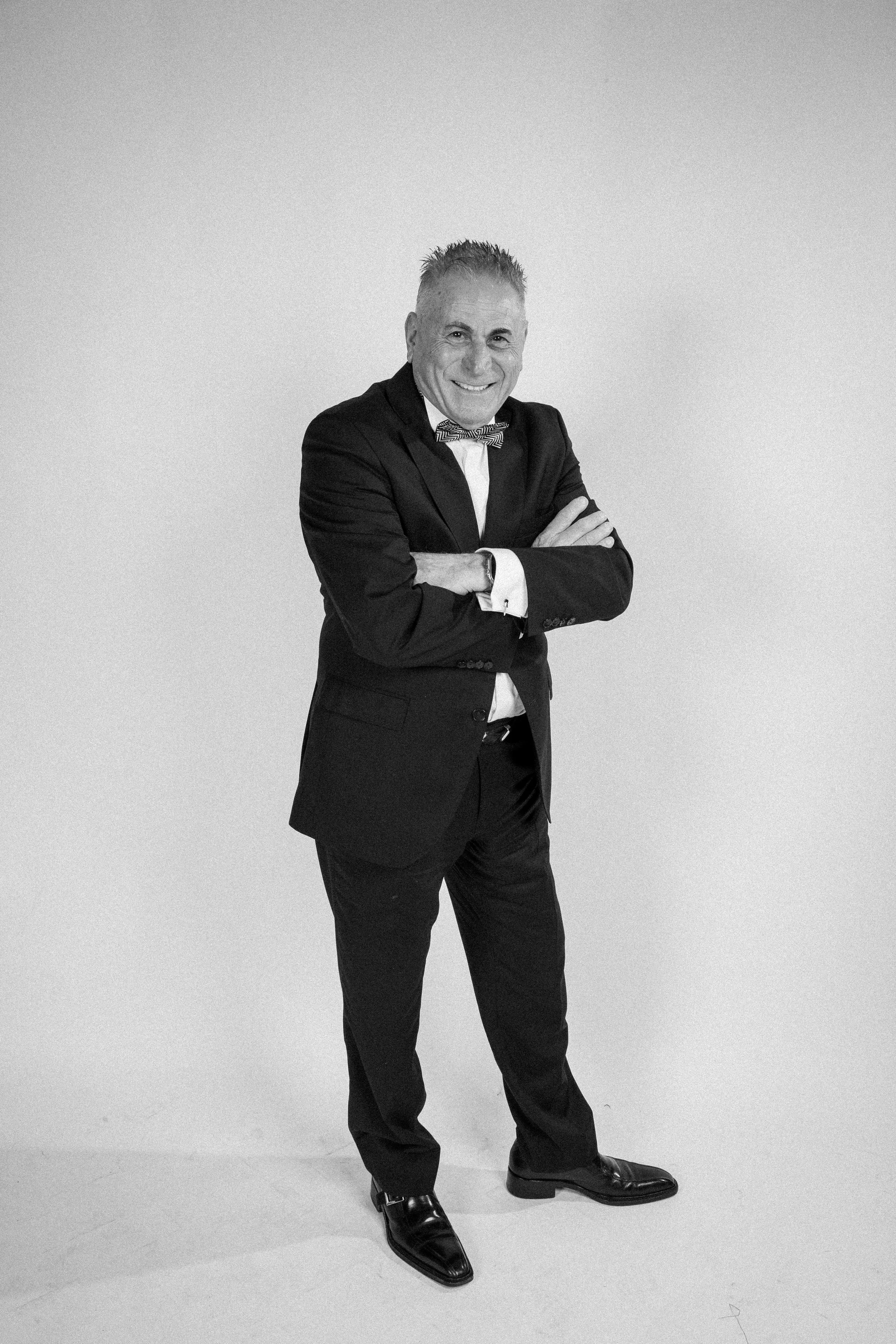 Solo portrait of a man in a suit standing confidently with arms crossed in front of a white paper infinity wall.